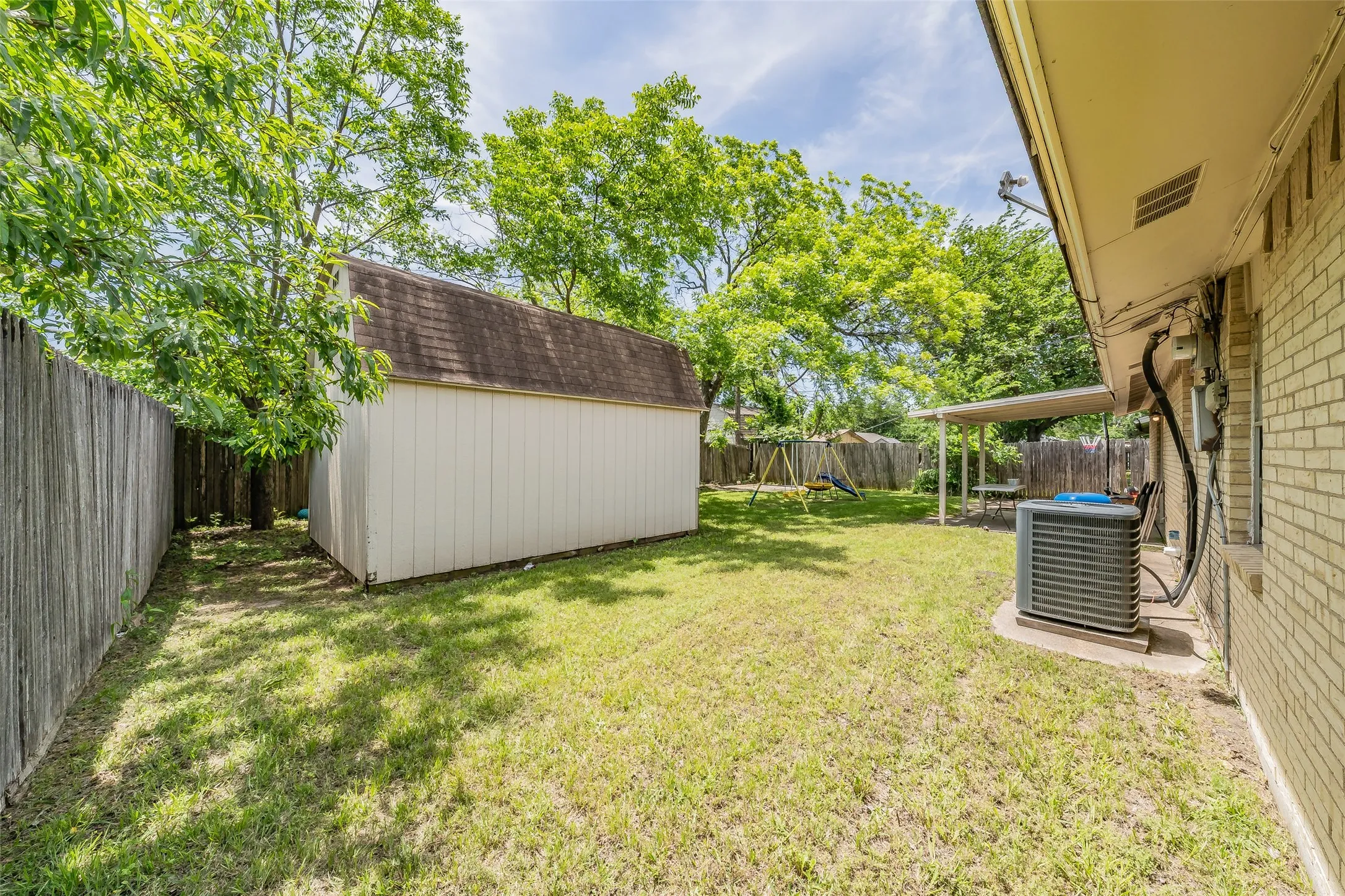 Storage shed and shade trees in backyard enclosed by wood privacy fence.