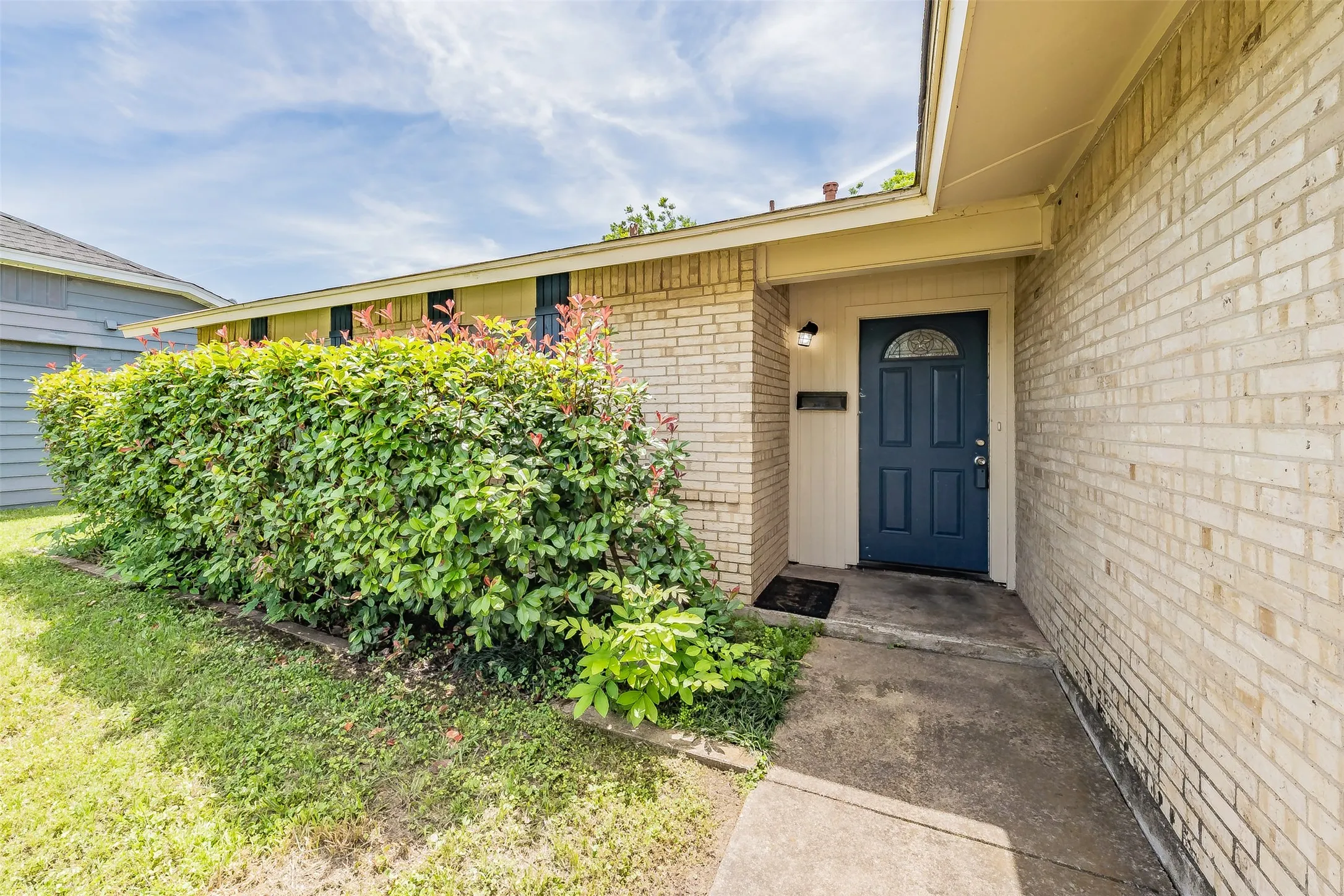 Cream brick exterior featuring a dark blue front door with an arched window, complemented by a concrete walkway