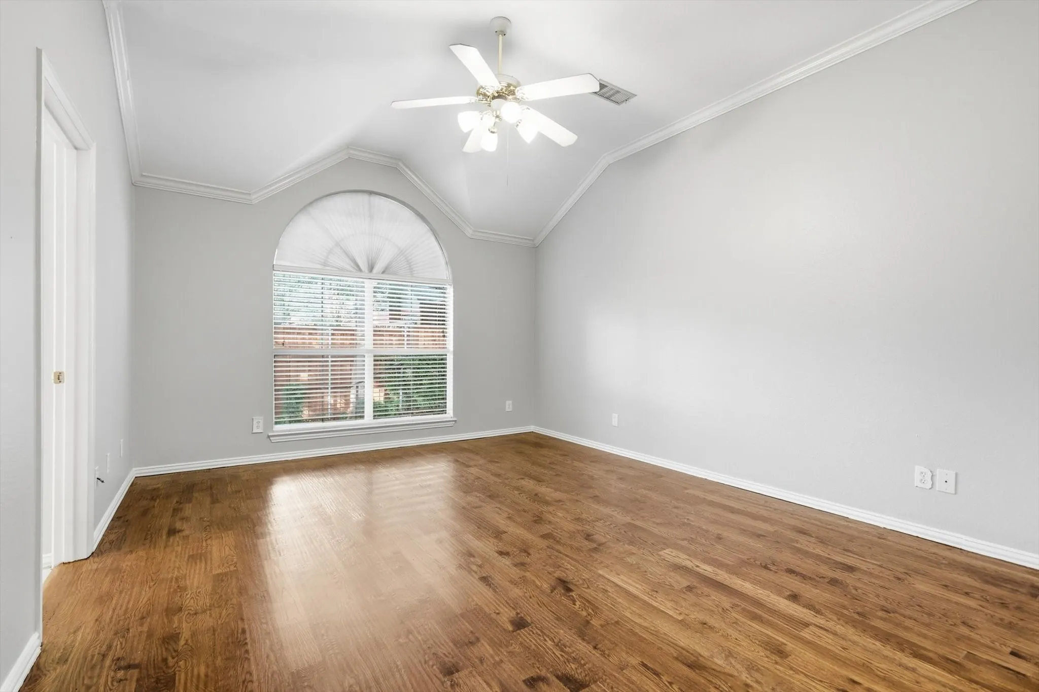 Vaulted ceiling room featuring wood-finish flooring, an arched window with blinds, and a ceiling fan with light fixture