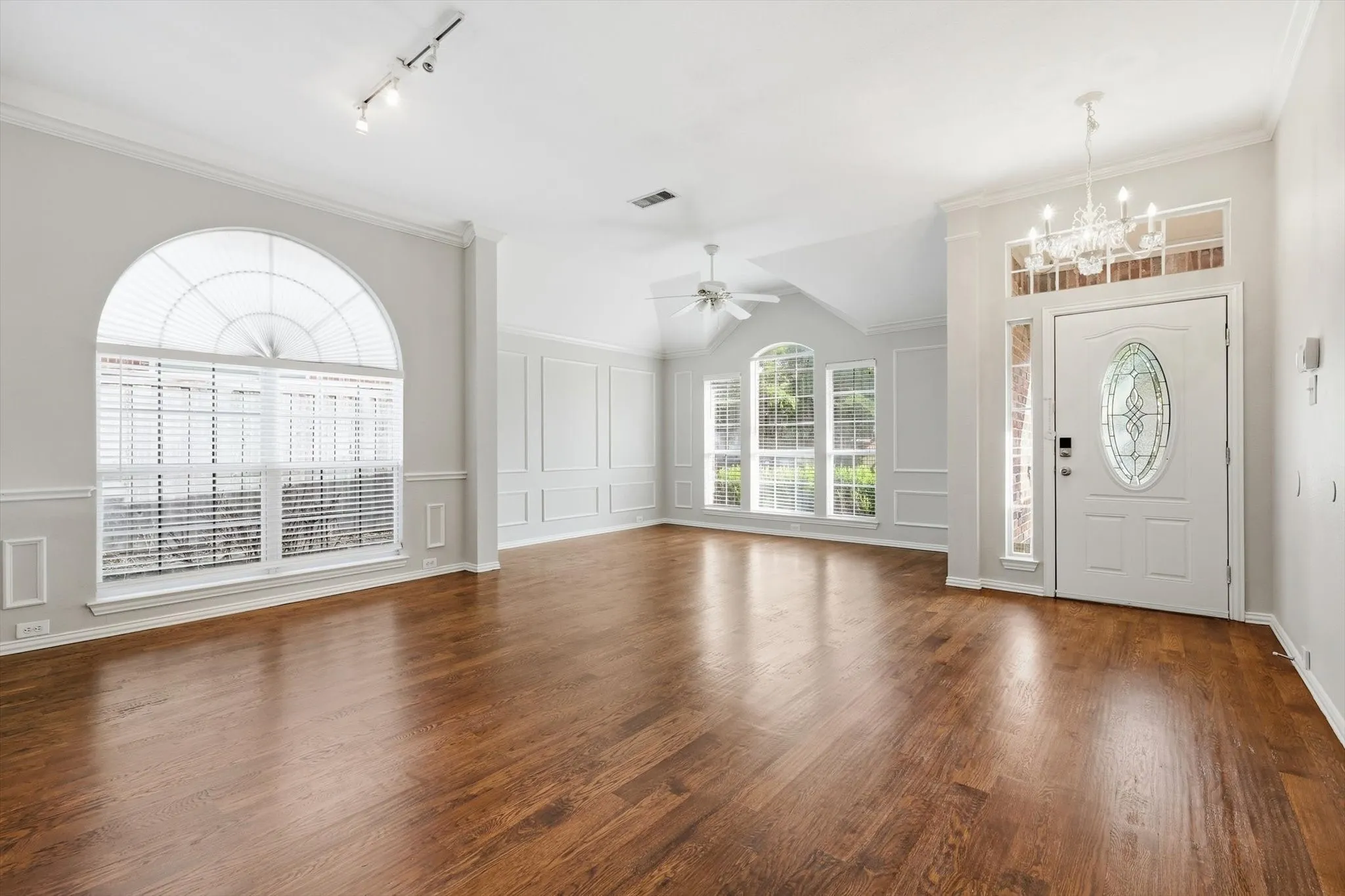 Entryway and living area featuring wood-finish flooring, an arched window with blinds, decorative wall paneling, a vaulted ceiling, and a white front door with an oval leaded glass insert