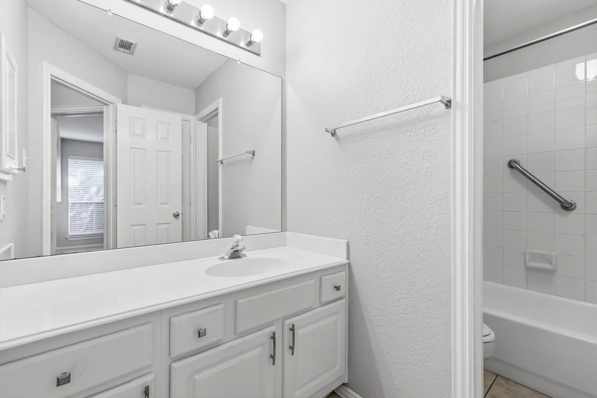 Bathroom featuring a vanity with an integrated sink, a large wall-mounted mirror, a four-bulb vanity light fixture, and a bathtub with white subway tile surround