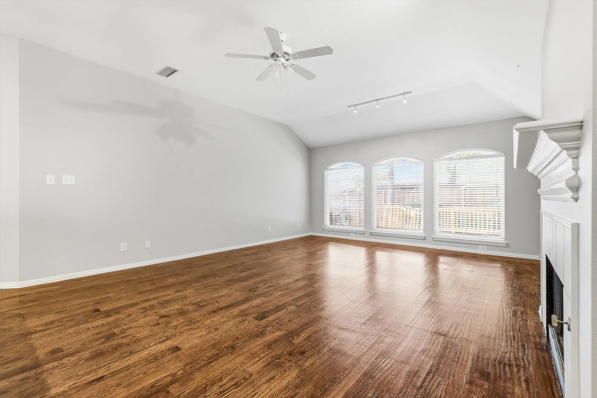 Spacious room featuring vaulted ceilings, wood-finish flooring, and a fireplace with a decorative mantel