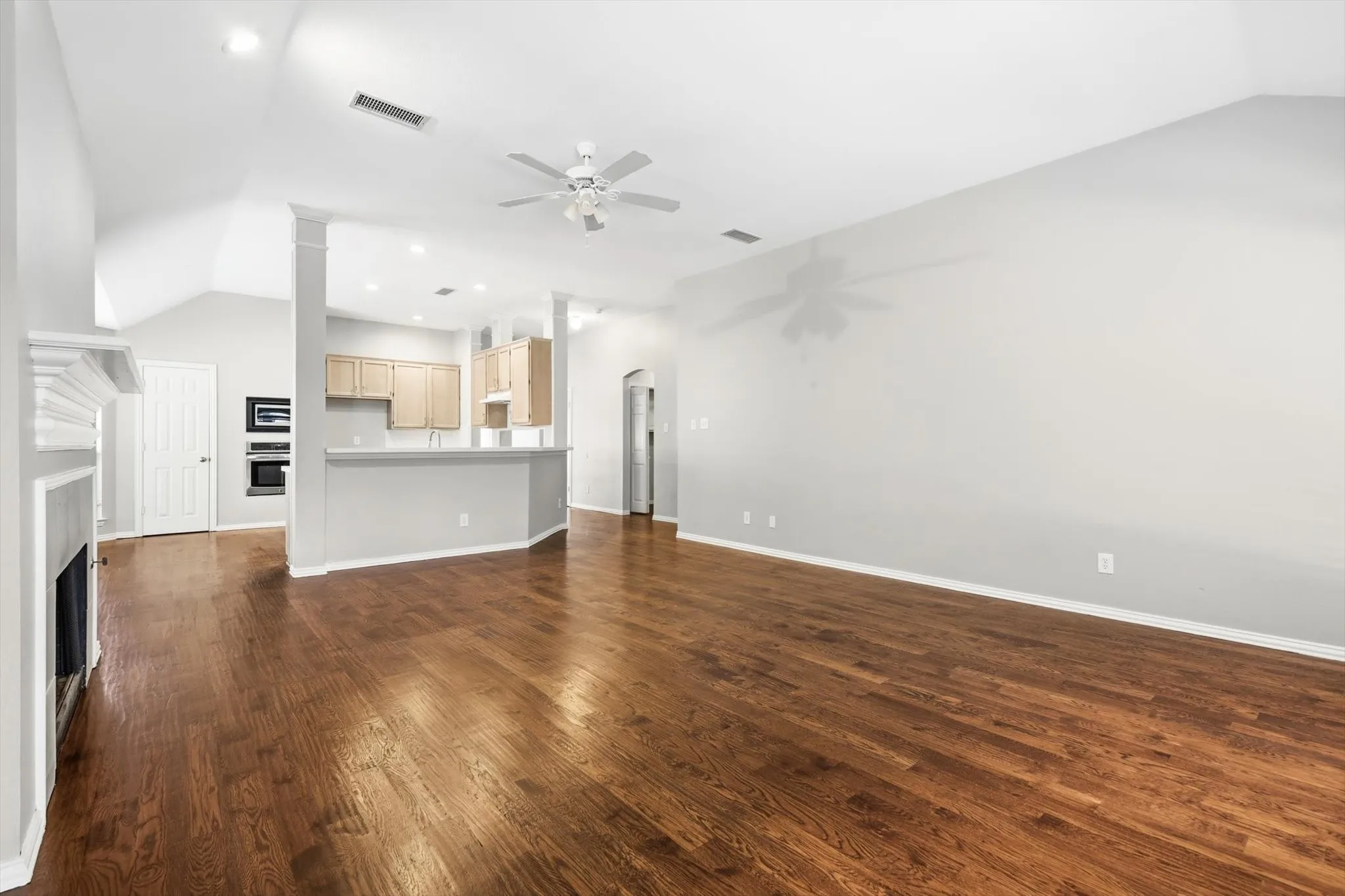 Spacious living area featuring wood-finish flooring, a white mantelpiece, vaulted ceilings, and a ceiling fan