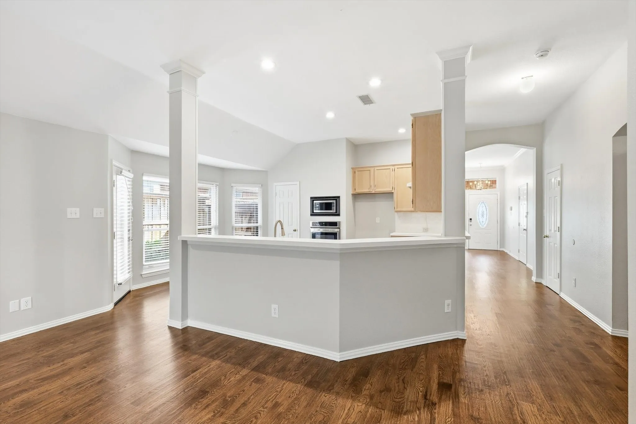 Open-concept living space featuring wood-finish flooring, a kitchen bar, light cabinetry, and an arched entryway