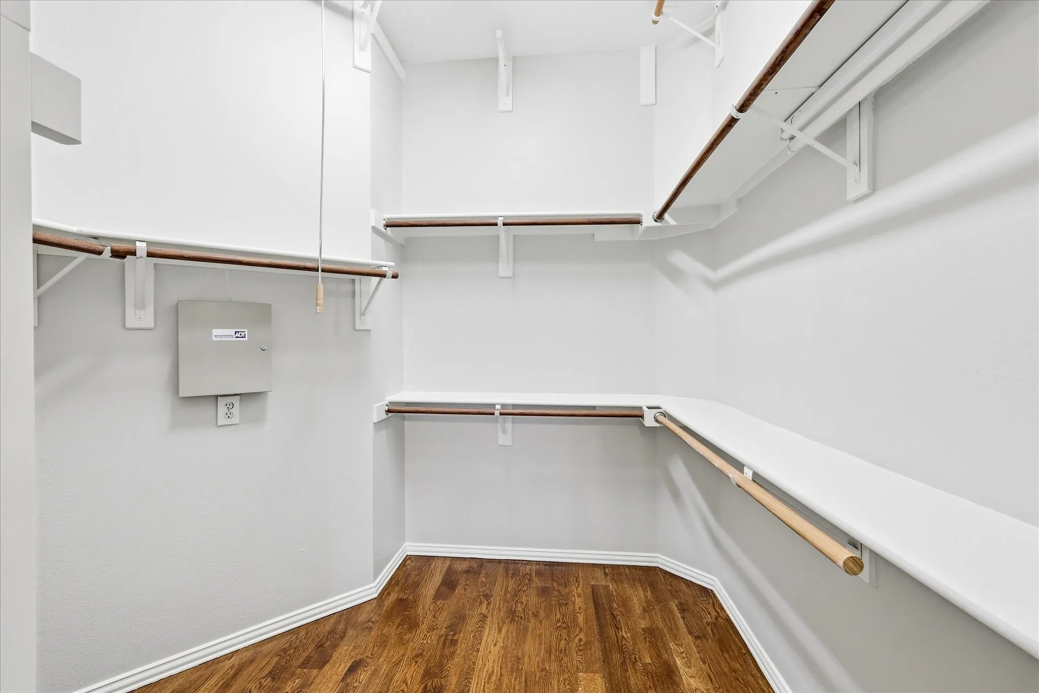 Walk-in closet featuring wood-finish flooring, white walls, white shelving, and hanging rods