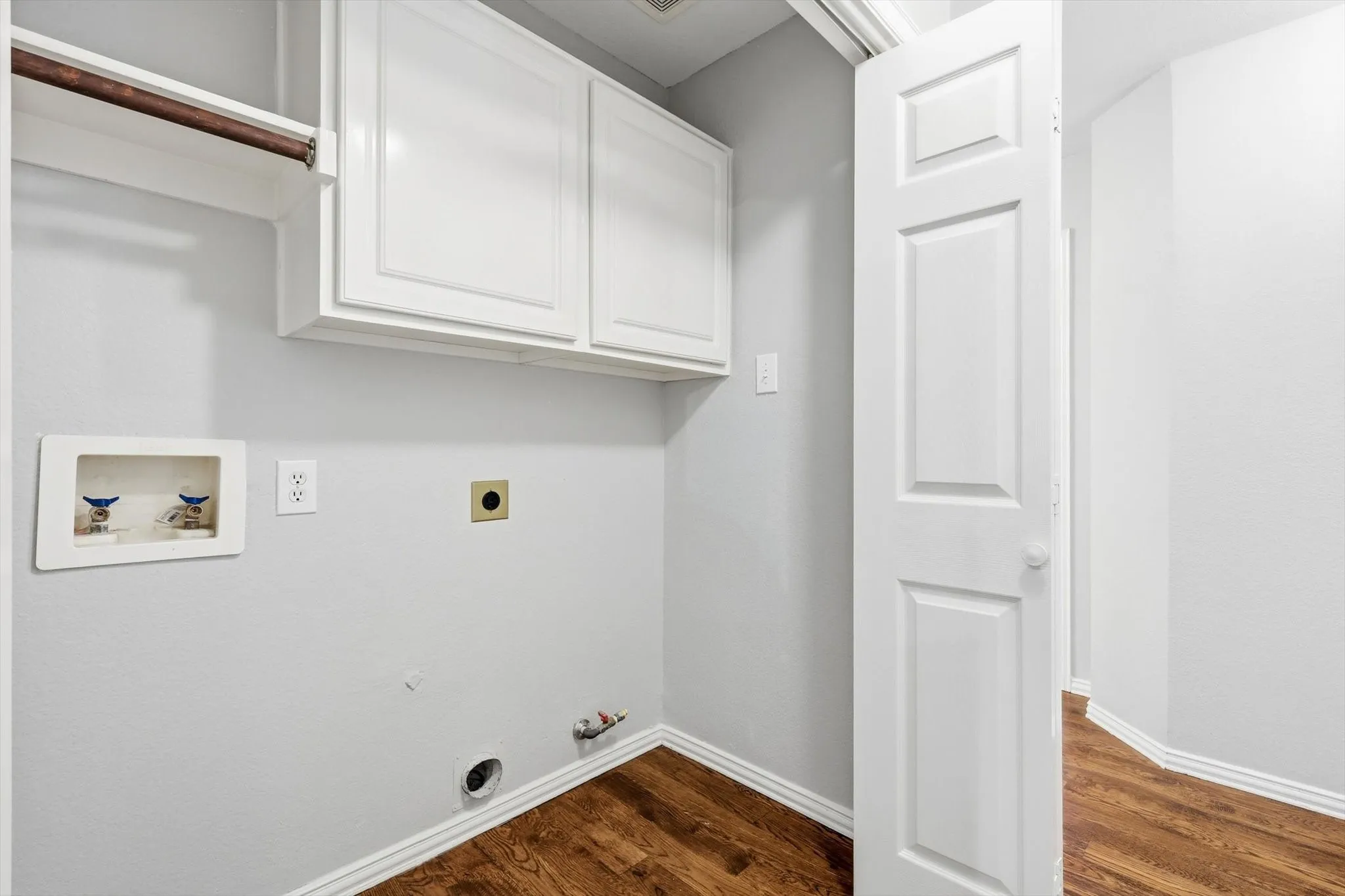 Dedicated laundry area featuring white shaker-style cabinetry, a built-in hanging rod, utility hookups, and wood-finish flooring