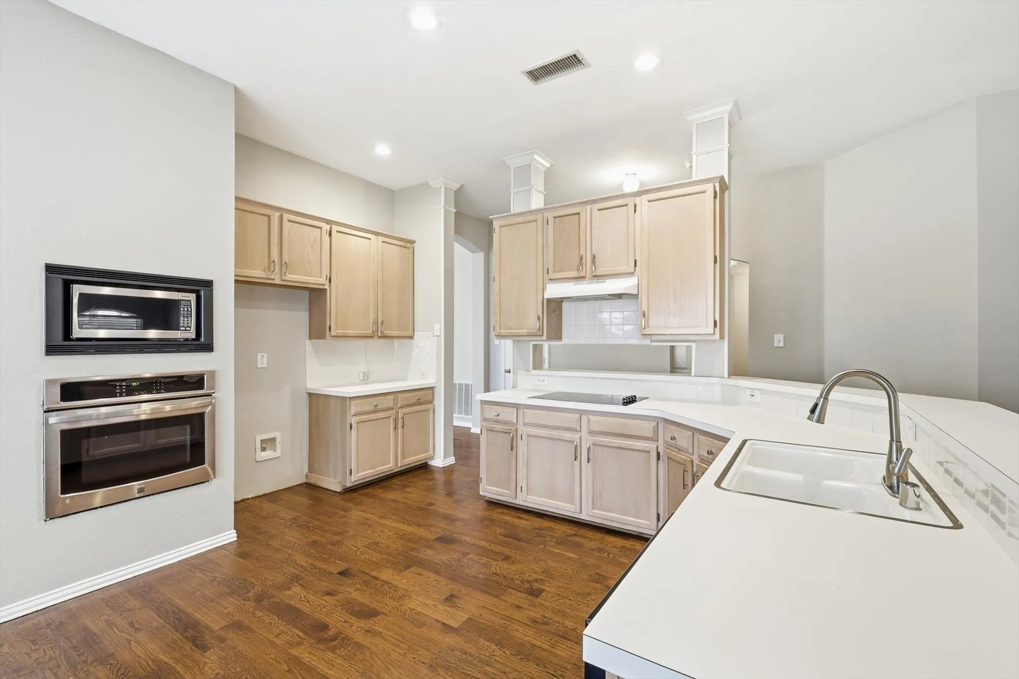 Kitchen featuring wood-finish flooring, light-toned cabinetry, white countertops, built-in microwave, and stainless steel oven