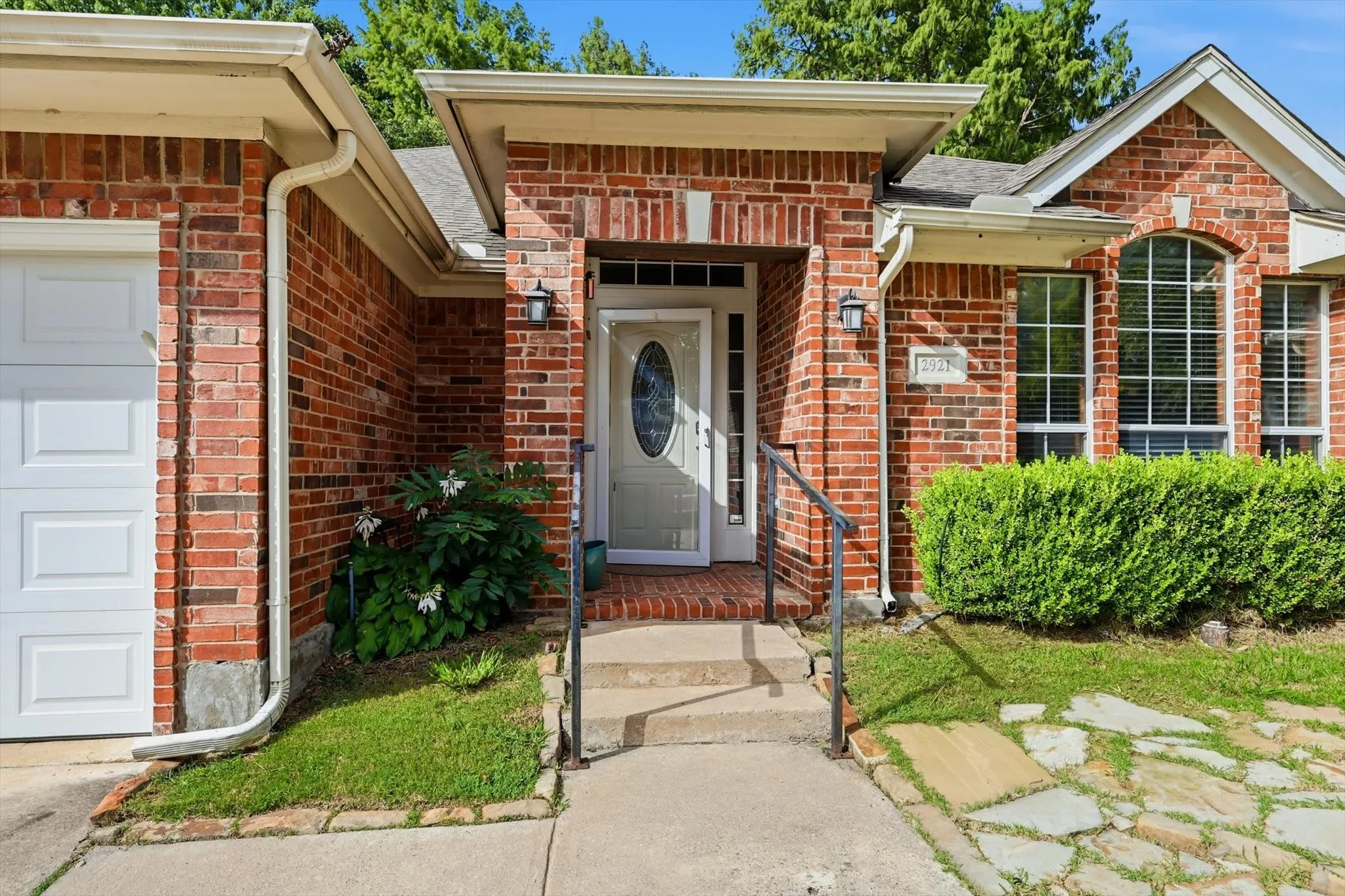 Brick exterior featuring a white garage door, a white entry door with oval glass, an arched window, and a stone walkway