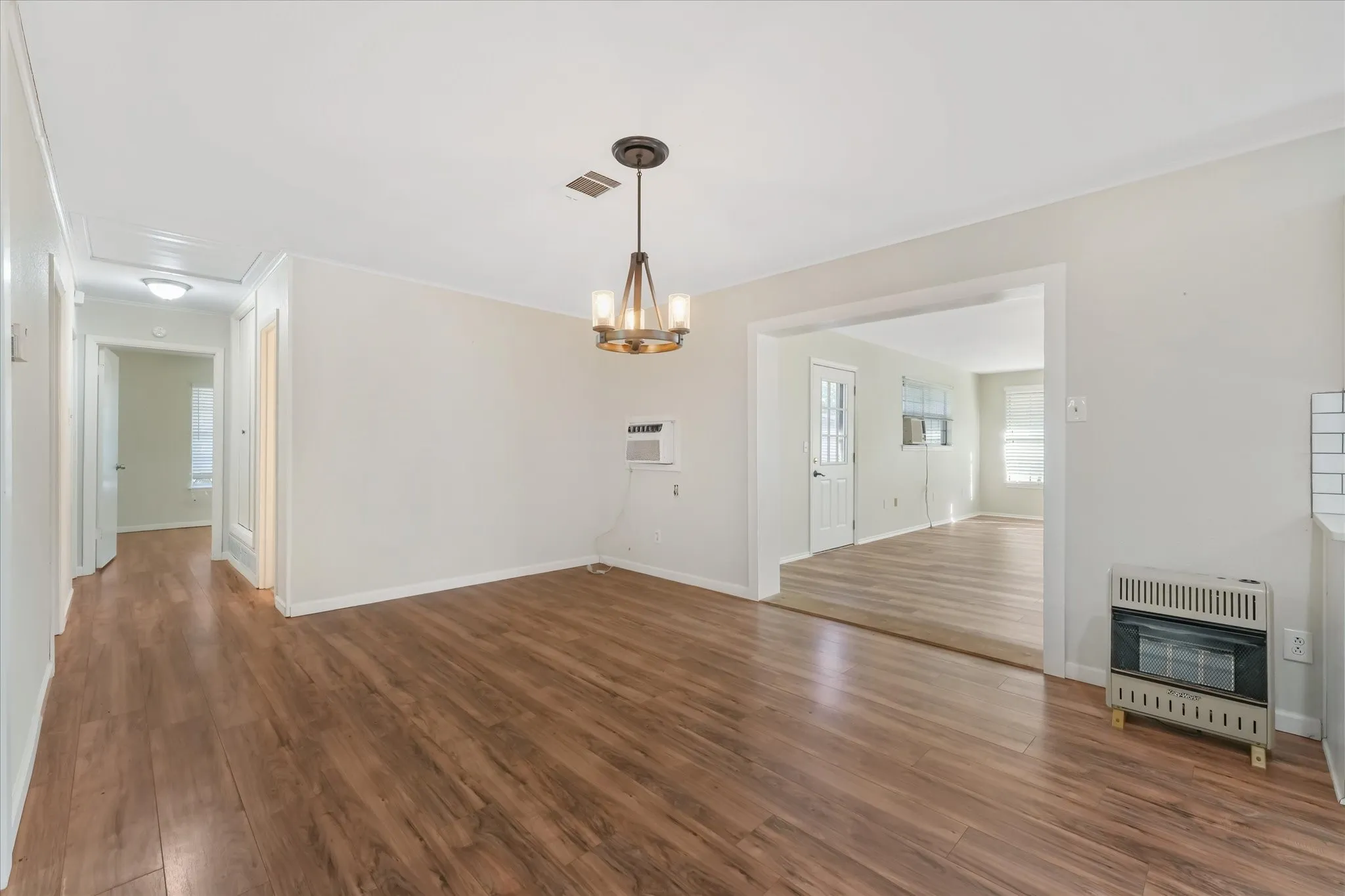 Unfurnished living room with dark wood-type flooring, heating unit, and a chandelier