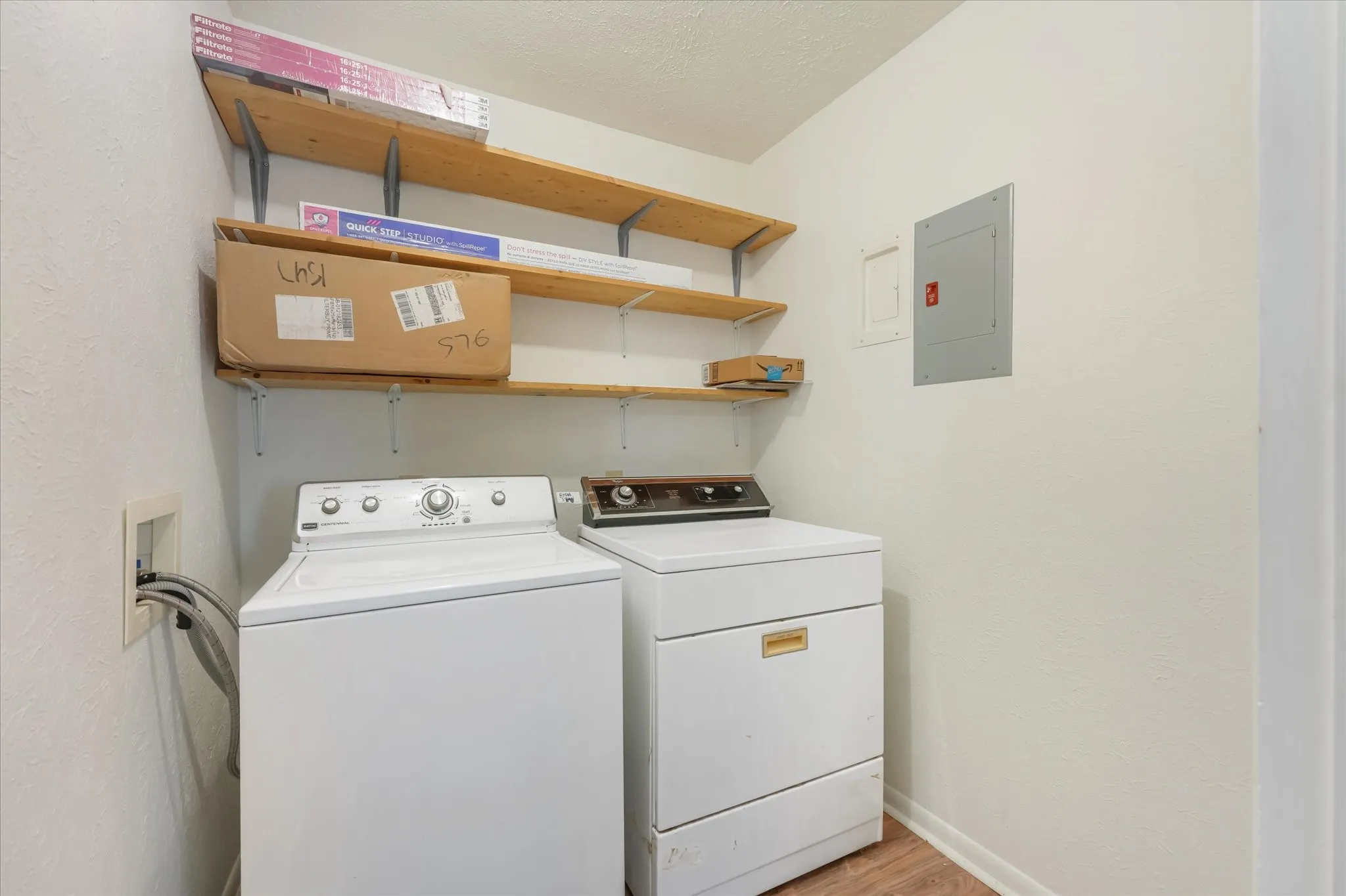 Washroom featuring a textured wall, electric panel, light wood finished floors, washing machine and dryer, and a textured ceiling