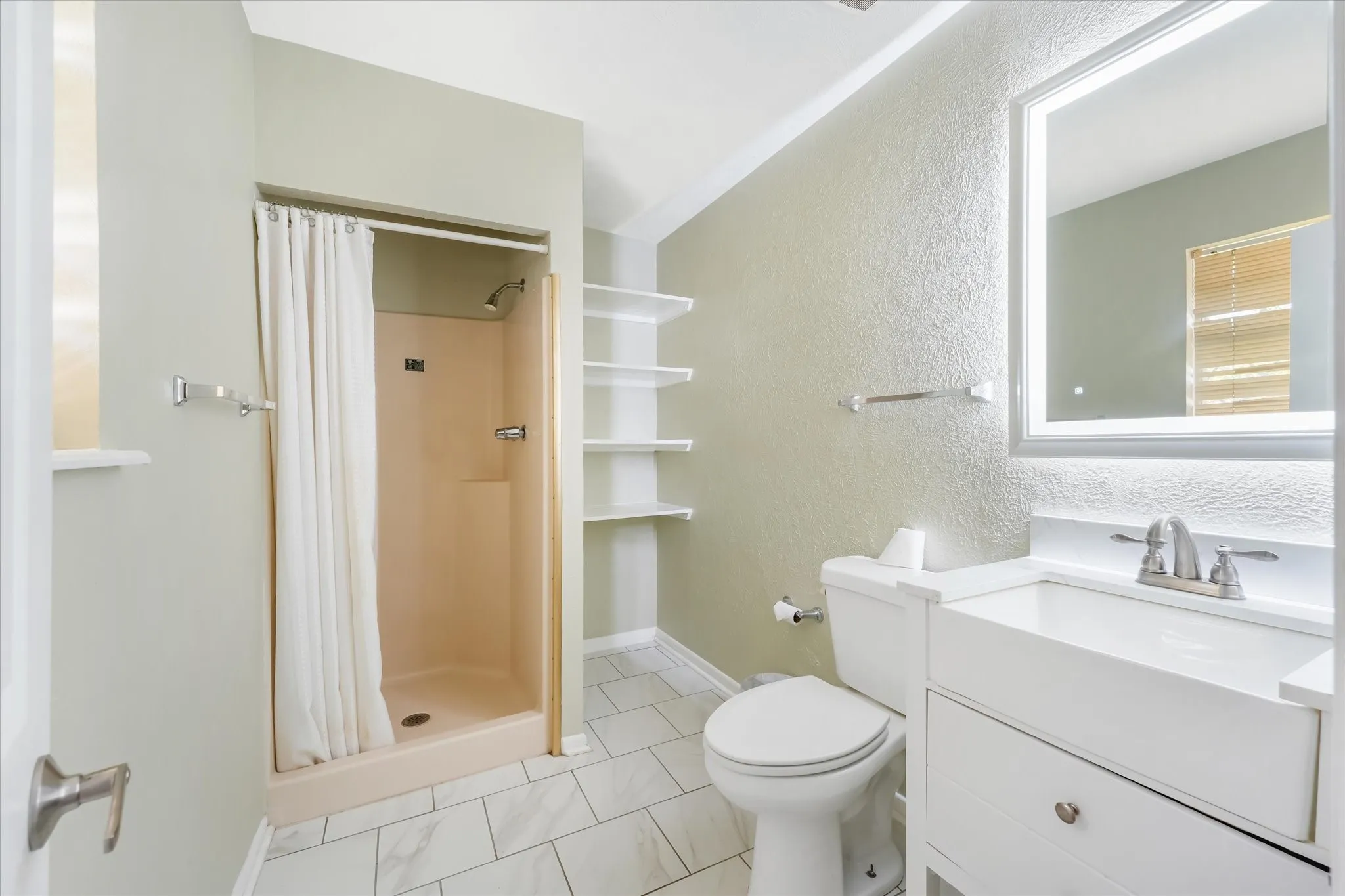 Full bathroom with a shower stall, a textured wall, vanity, and light tile patterned floors