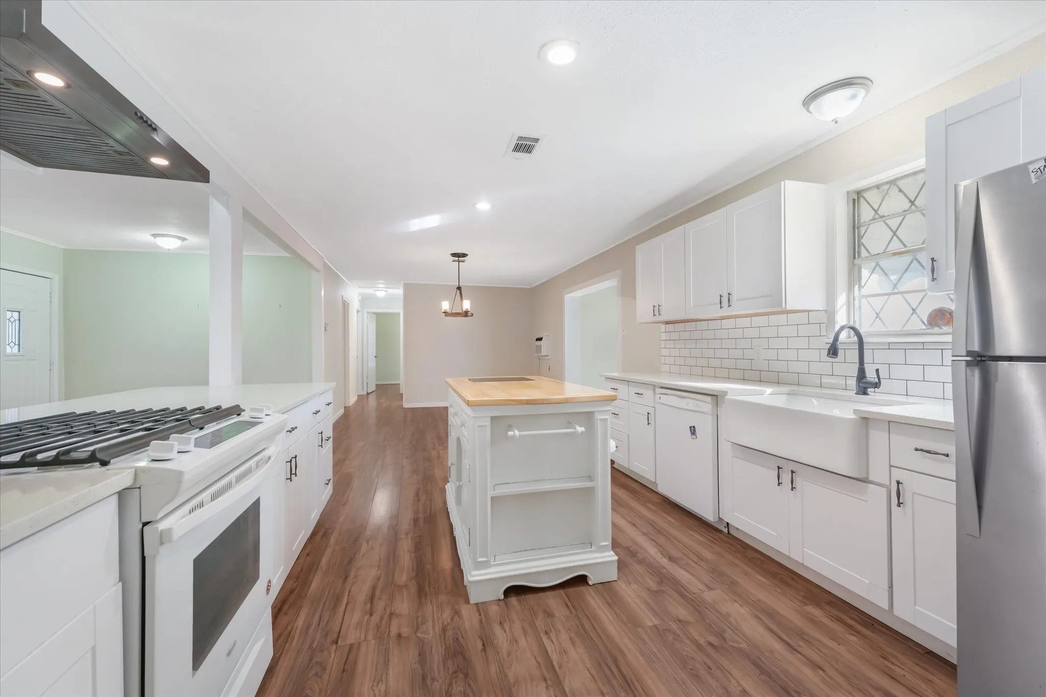 Kitchen featuring white appliances, butcher block counters, ventilation hood, white cabinets, and dark wood-style floors