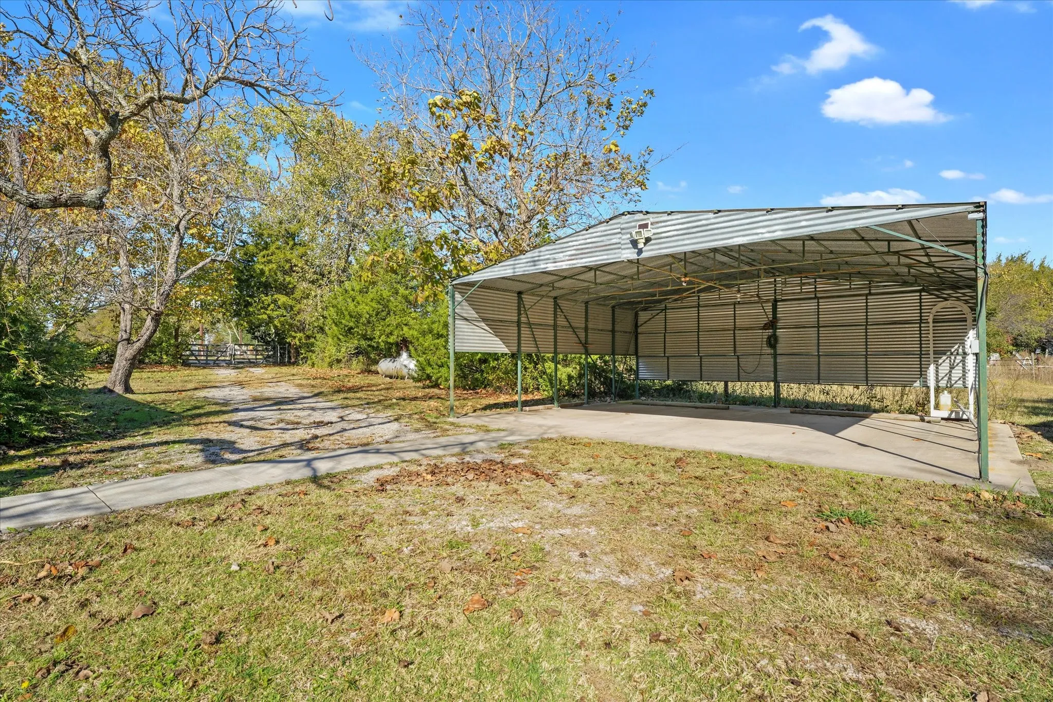 View of green lawn featuring a detached carport and driveway