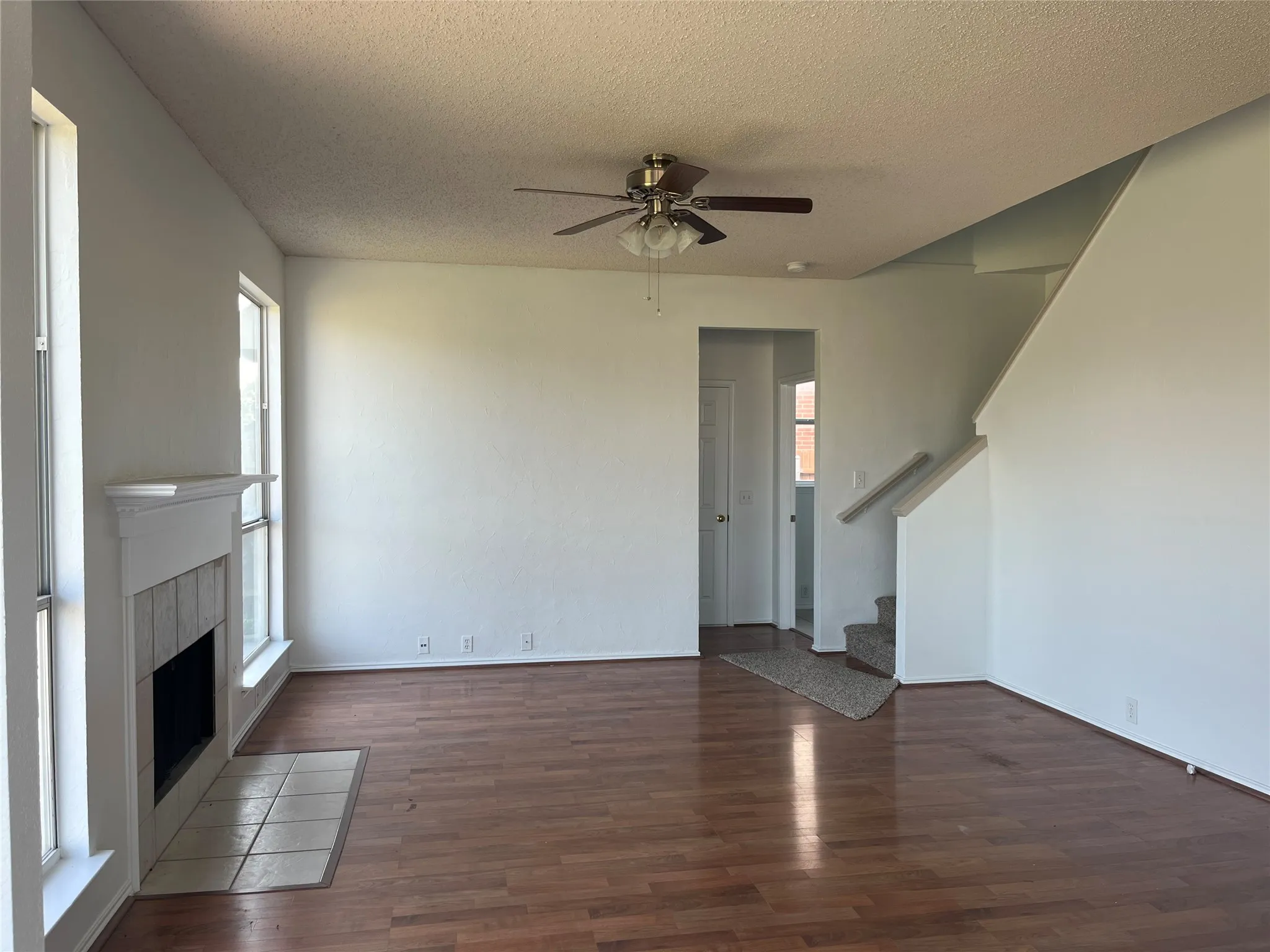 Spacious interior featuring wood-finish flooring, a ceiling fan, and a fireplace with a white mantel and tile hearth