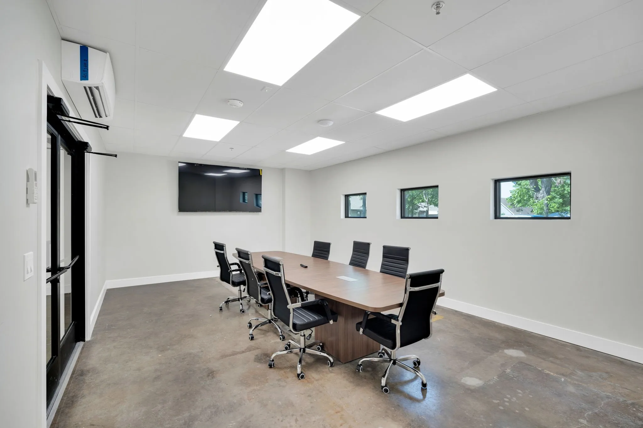 Bright room featuring a large mounted display, multiple rectangular windows, and a black framed glass door
