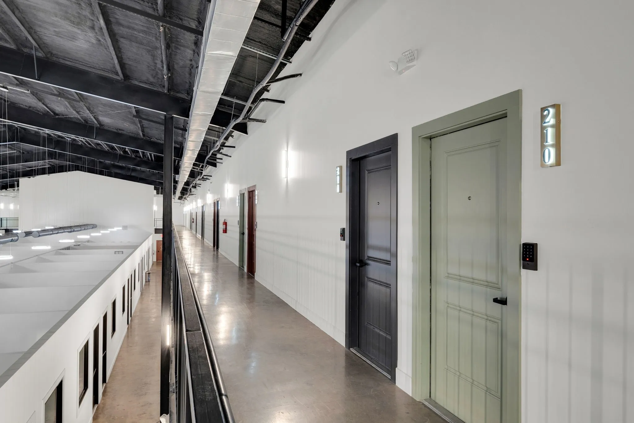 Industrial-style corridor featuring exposed ceiling joists, concrete flooring, and modern wall sconces