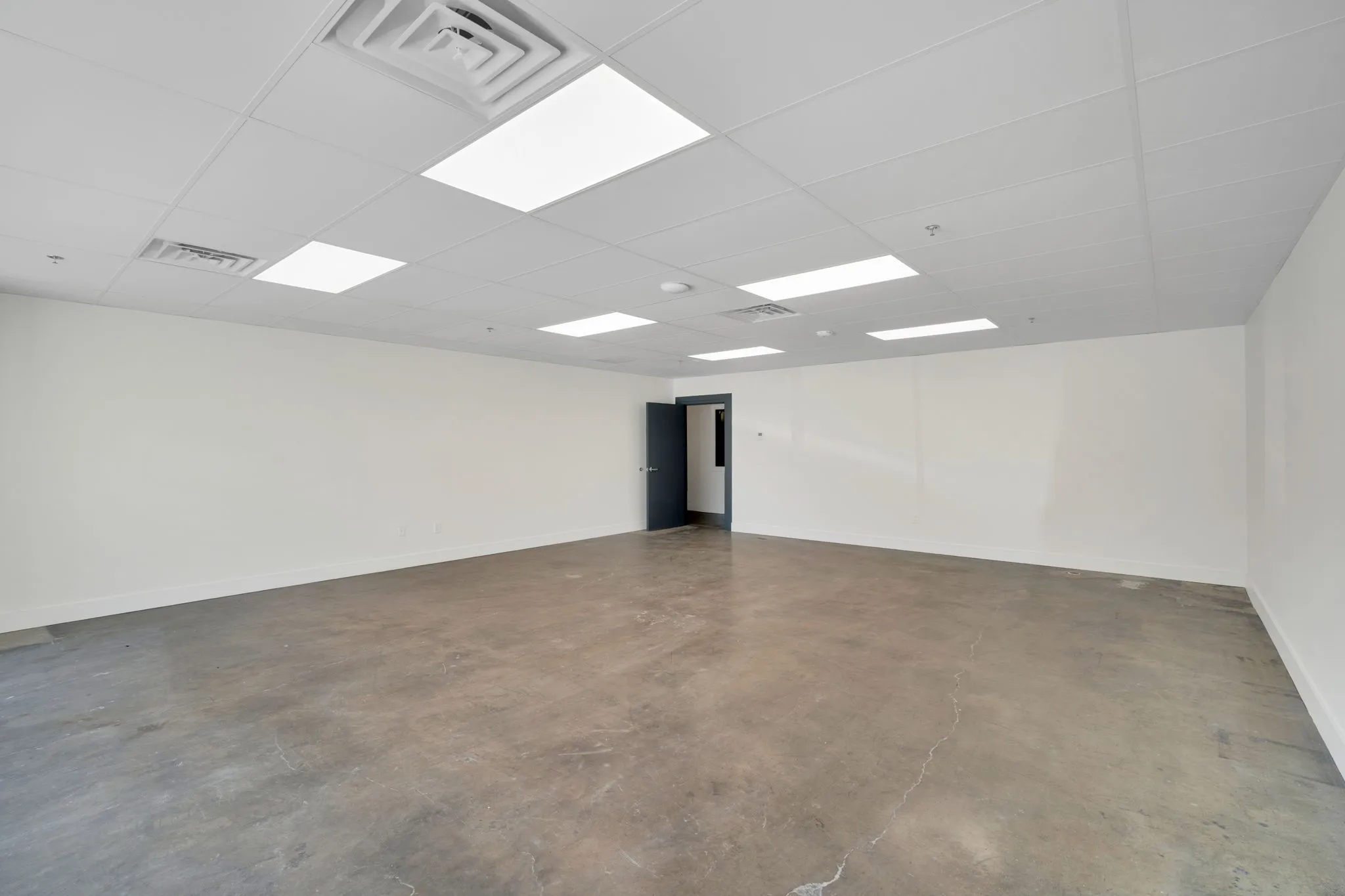 Spacious room featuring concrete flooring and a drop ceiling with integrated rectangular and square lighting fixtures
