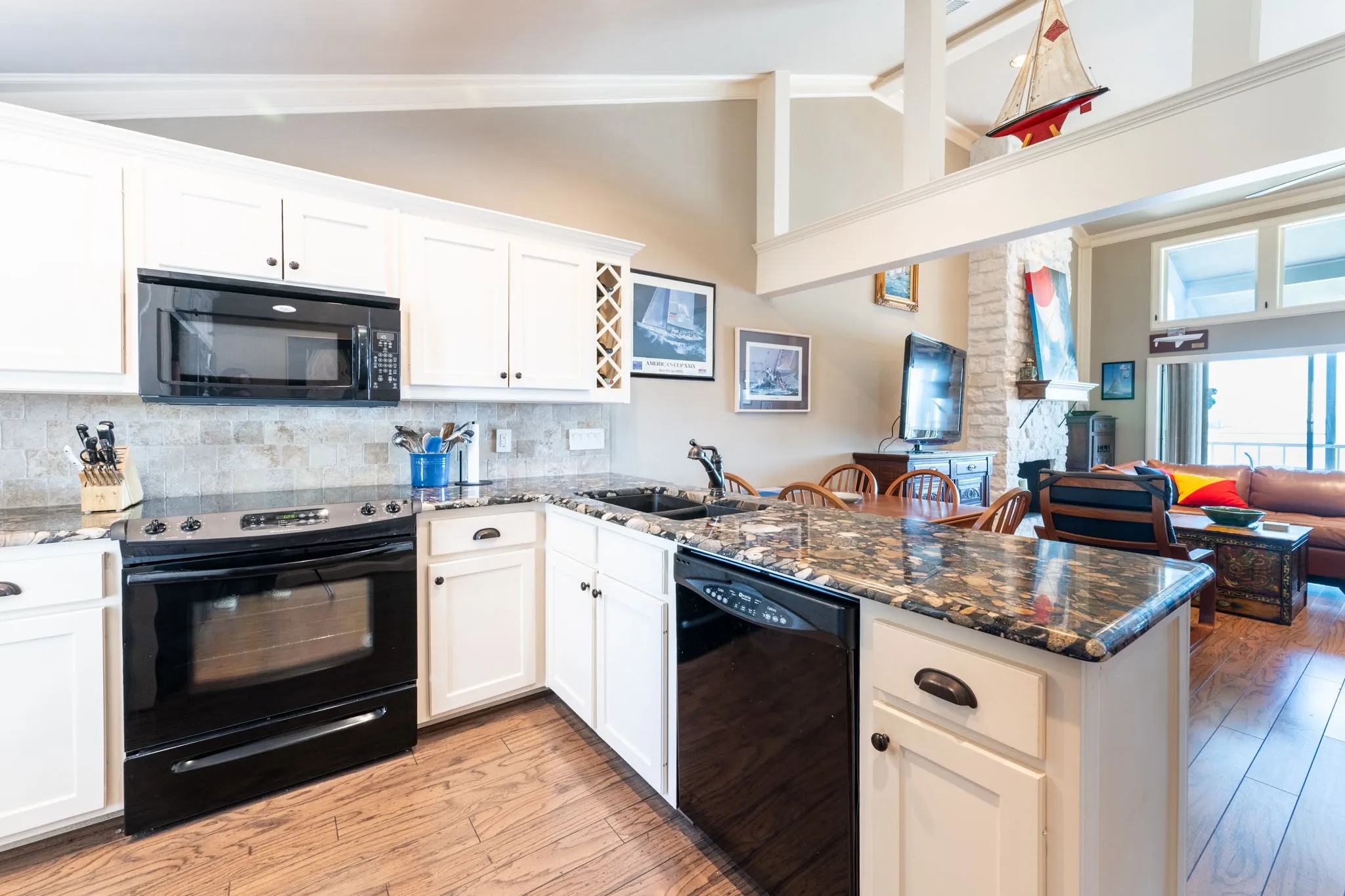 Kitchen featuring white cabinetry, black appliances, dark granite-look countertops, and wood-finish flooring
