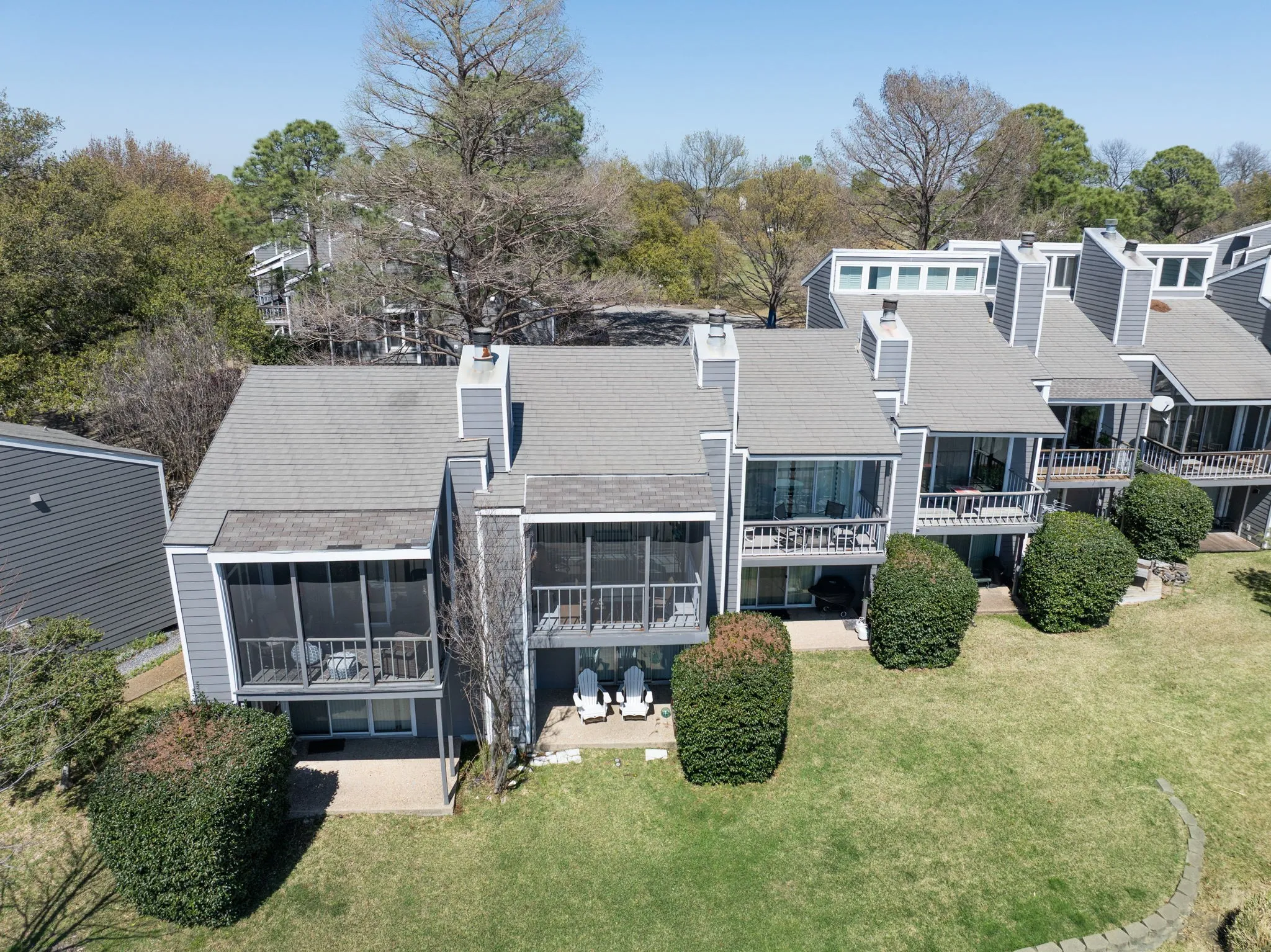 Rear exterior featuring multiple screened porches, private patio areas, gray siding, and a gabled roofline