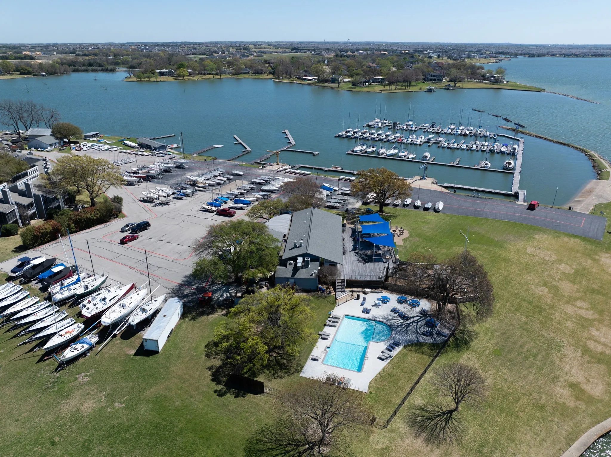 Expansive waterfront property featuring a large marina with multiple boat slips, a swimming pool with surrounding lounge chairs, and a spacious green lawn