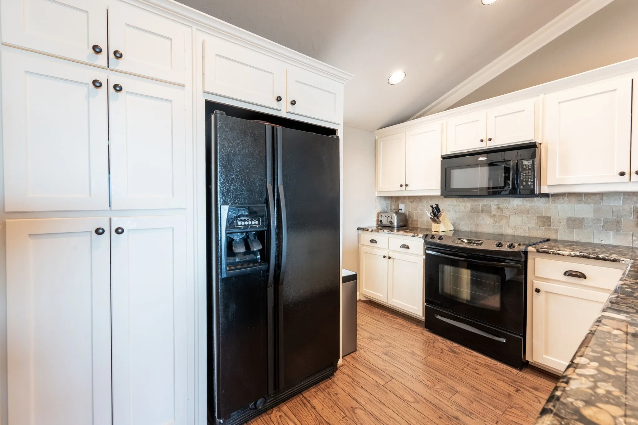 Kitchen featuring white shaker-style cabinetry, dark granite countertops, and a stone tile backsplash