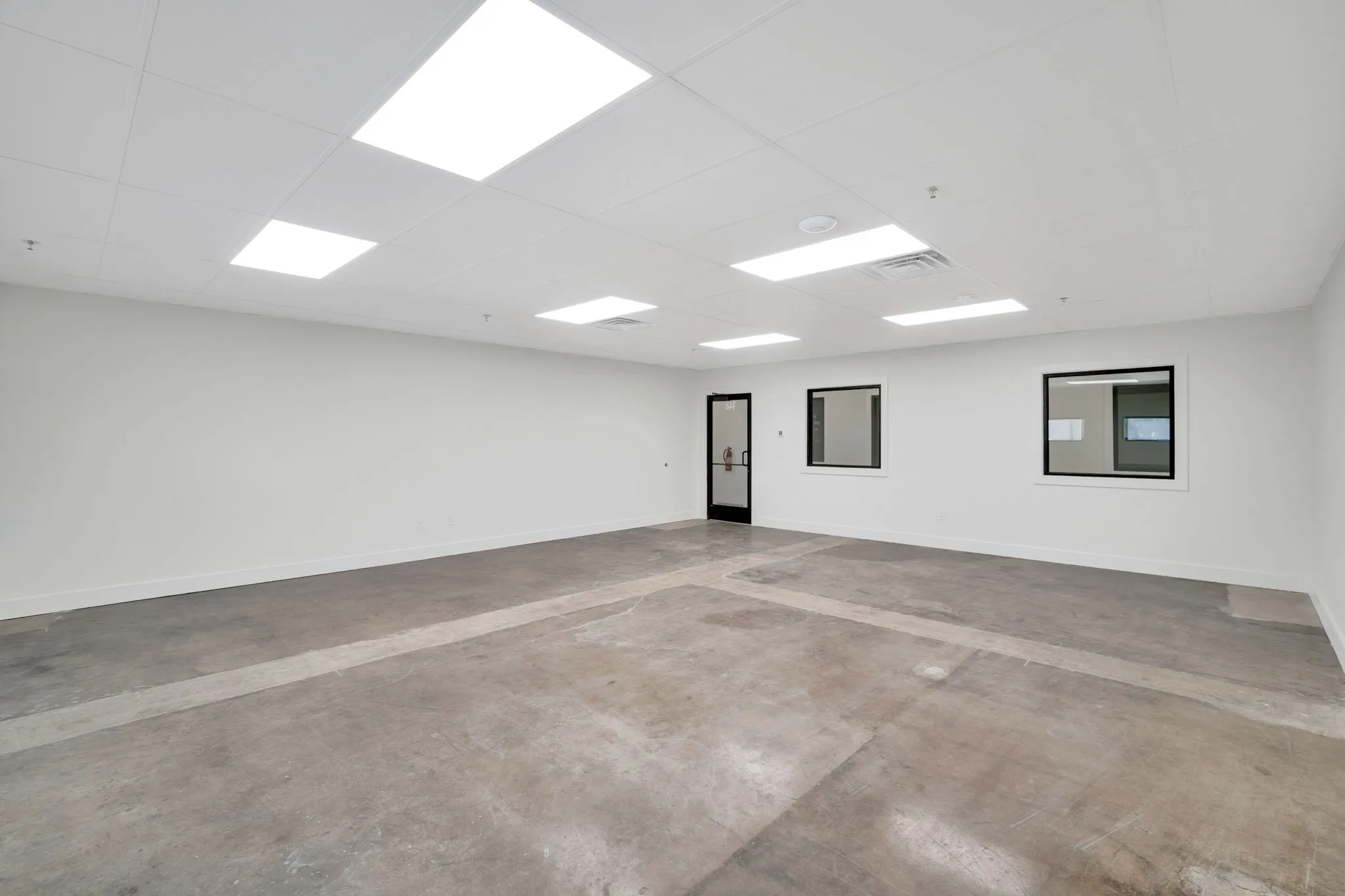 Expansive open-concept room featuring concrete flooring, a white drop ceiling with recessed lighting, and white painted walls