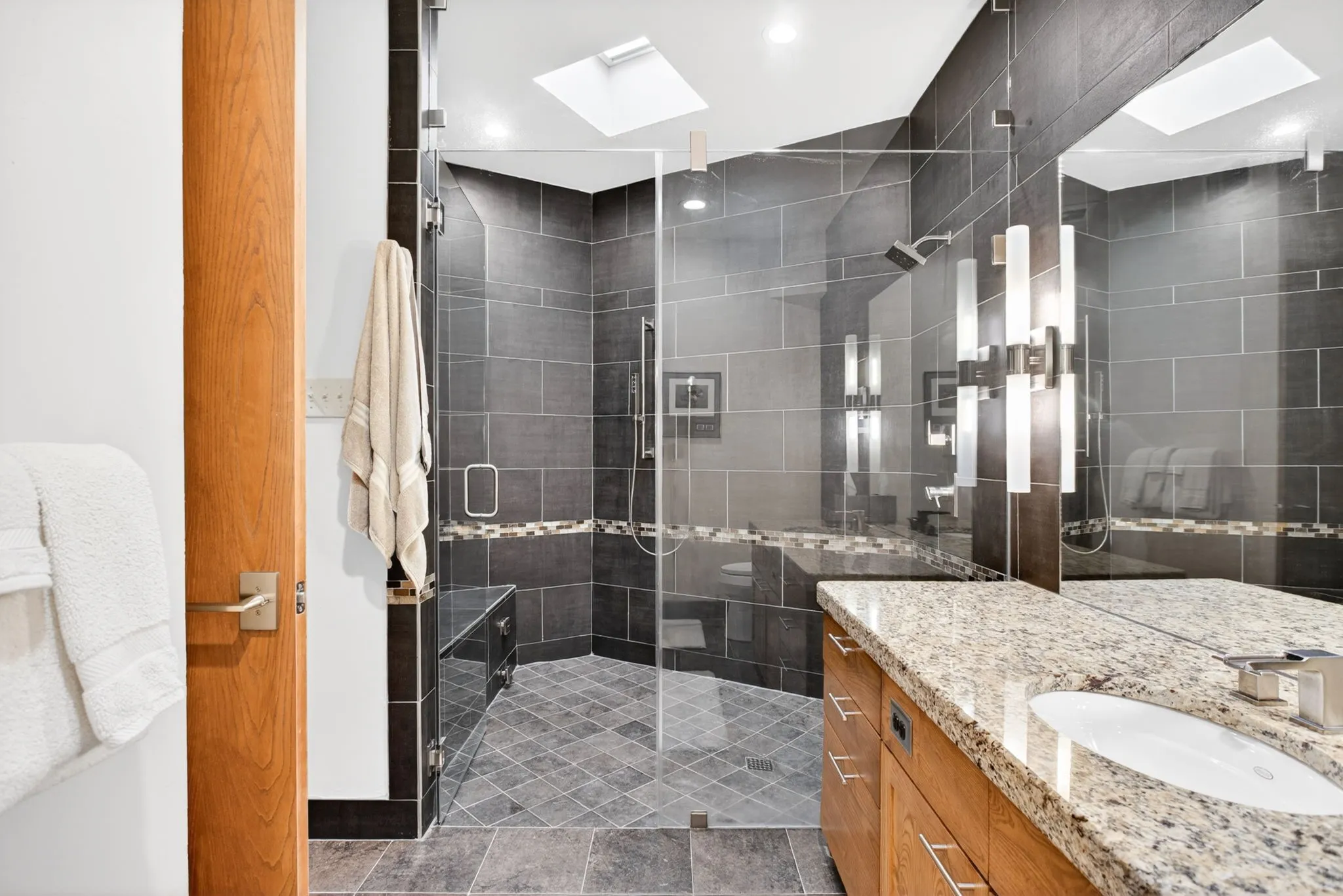 Spacious bathroom featuring a glass-enclosed shower with a built-in bench, a rain showerhead, and a​​‌​​​​‌​​‌‌​‌‌​​​‌‌​‌​‌​‌​​​‌​​ skylight