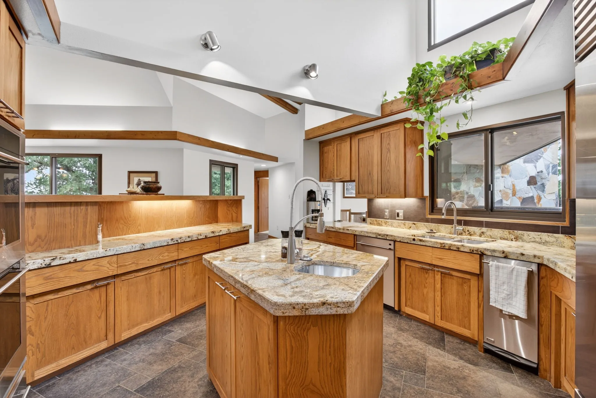 Kitchen featuring a hexagonal island with an undermount sink, light wood-finish cabinetry, stone countertops, and stainless steel appliances