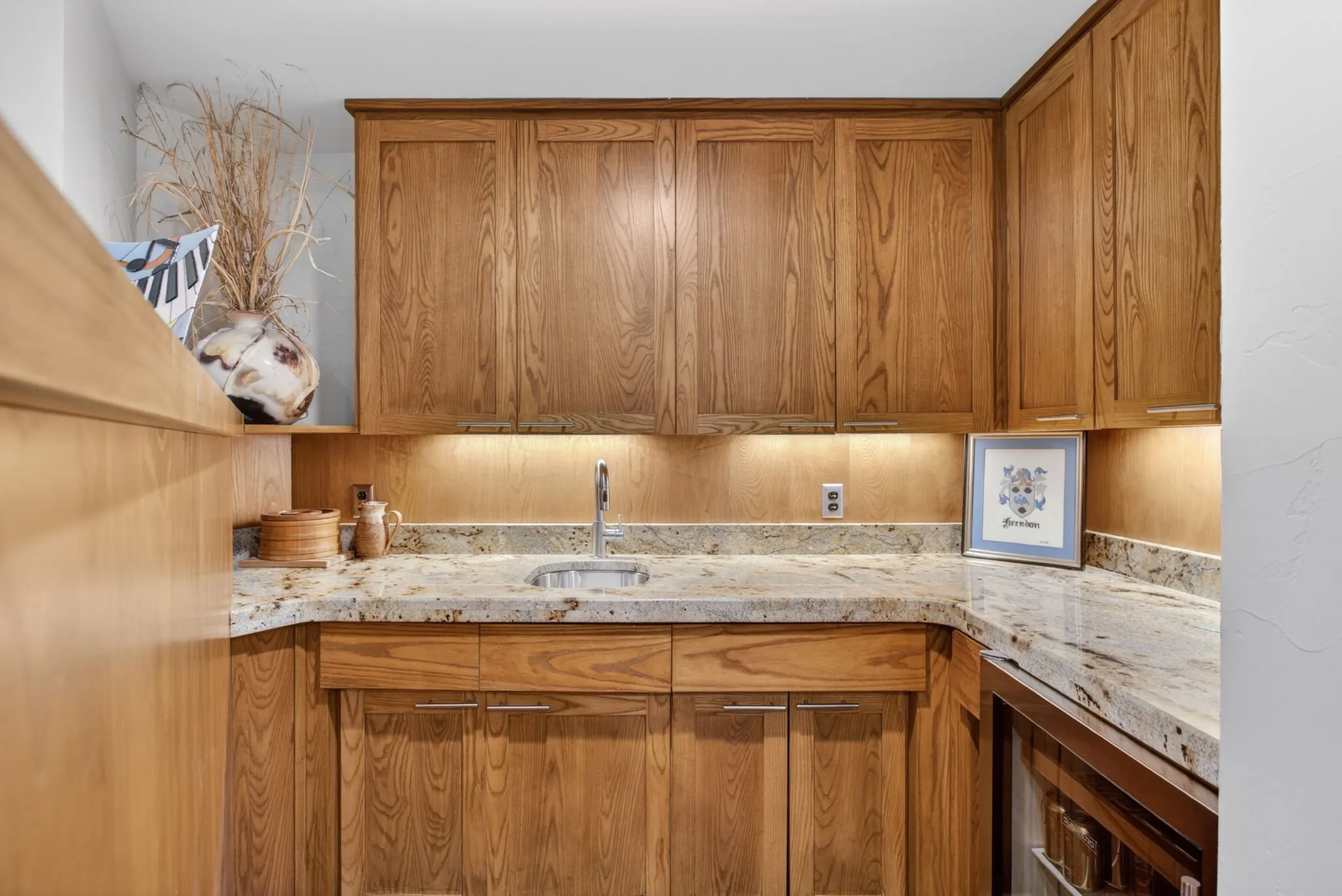 Custom Wet bar area with cabinetry with brushed nickel hardware, light granite countertops, stainless steel sink with gooseneck faucet, and integrated under-cabinet lighting