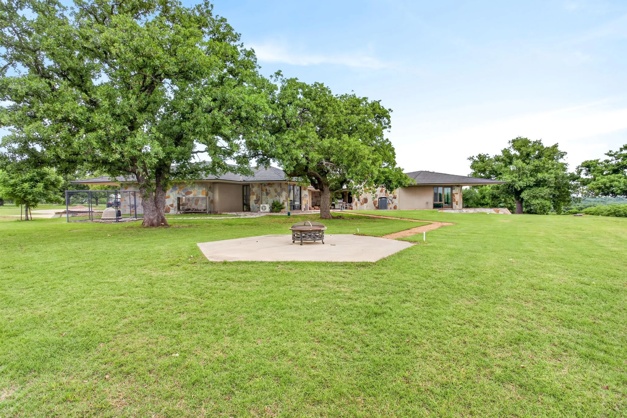 Expansive green lawn surrounds a stone-accented property with mature trees