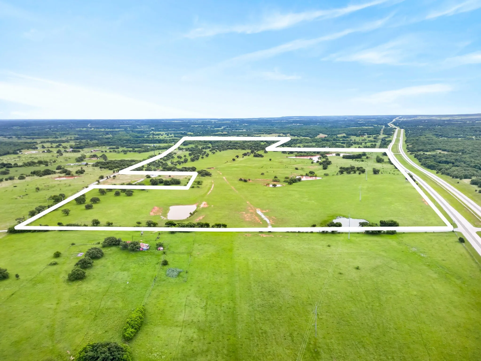 Expansive acreage featuring green pastures, mature trees, two ponds, and highway frontage