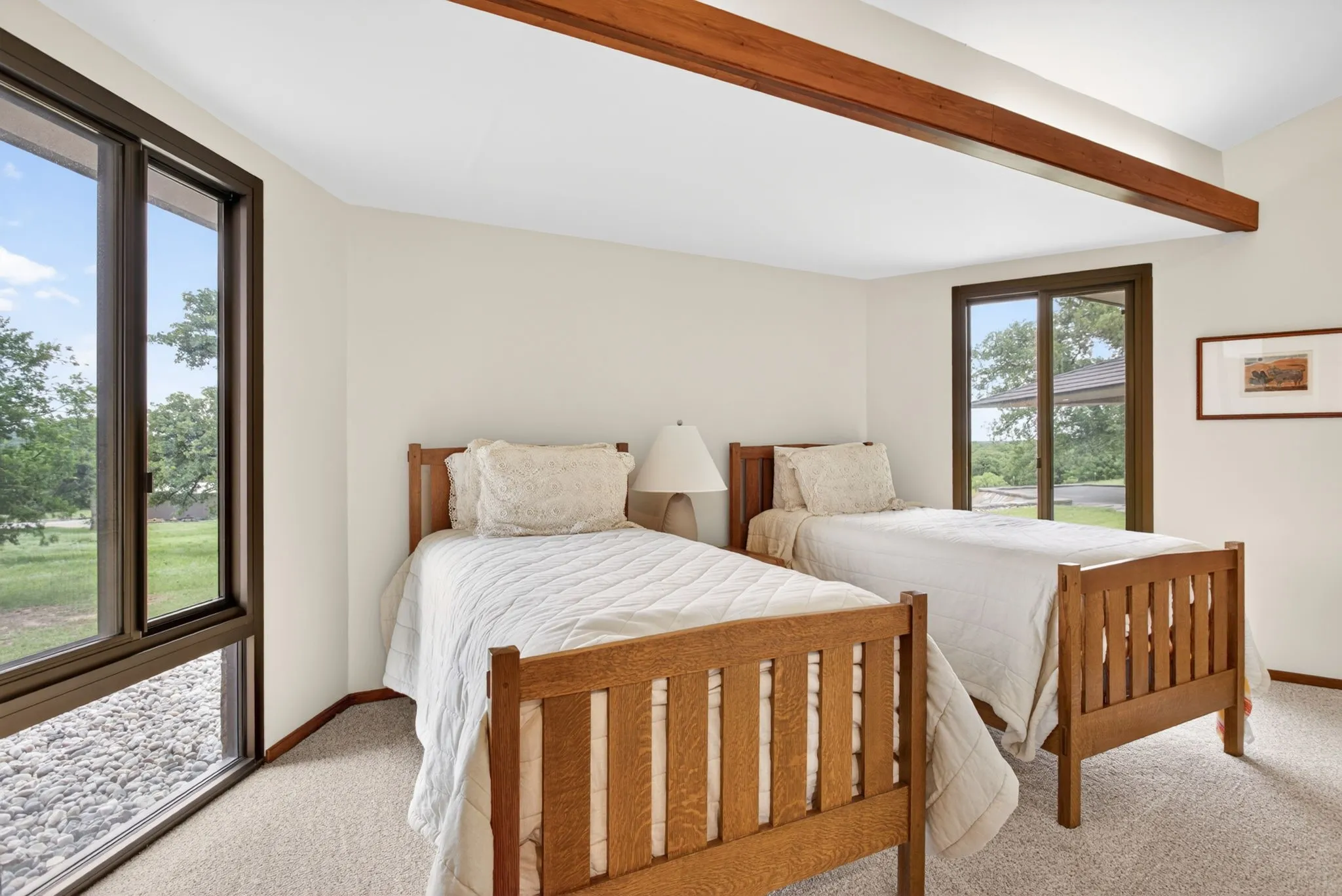 Carpeted room featuring a prominent exposed wood beam, multiple large windows with dark frames, and light-toned walls