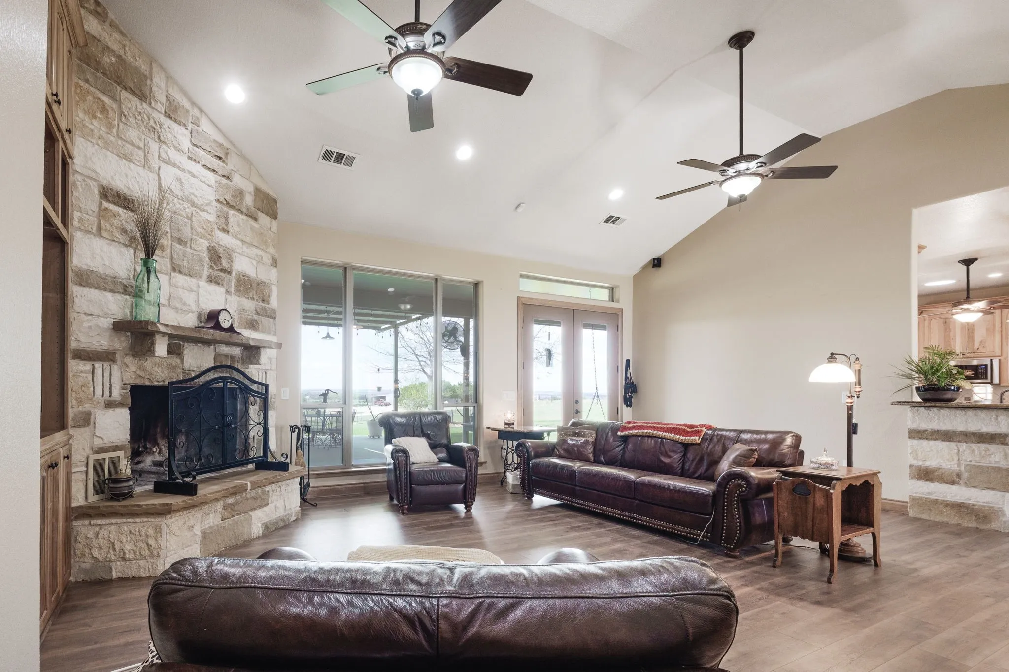 Spacious living area featuring a stone-clad fireplace with mantel, vaulted ceilings, and wood-finish flooring