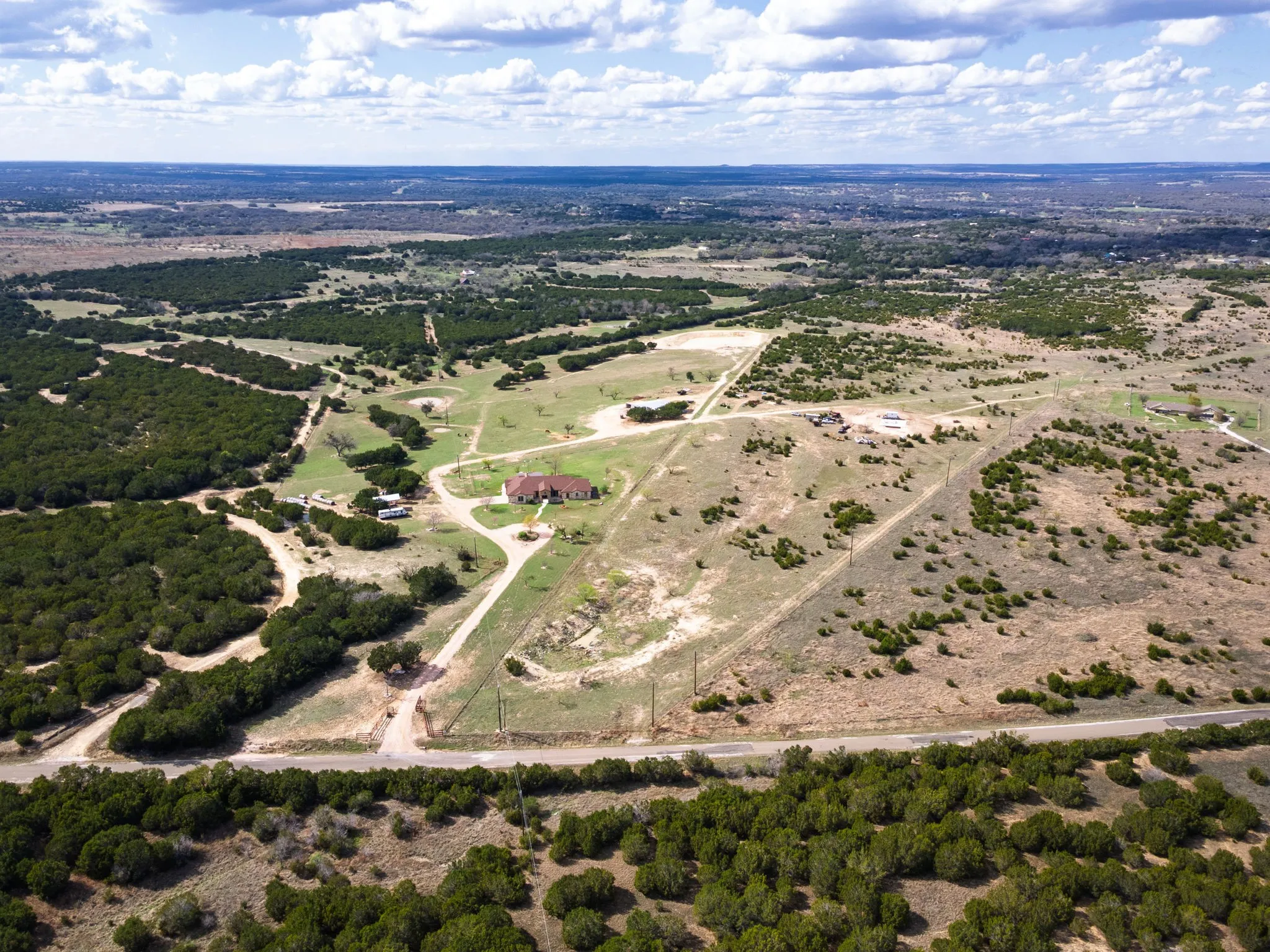 Expansive property featuring a red-roofed residence, extensive land, visible fencing, natural landscaping, and a clear roadway