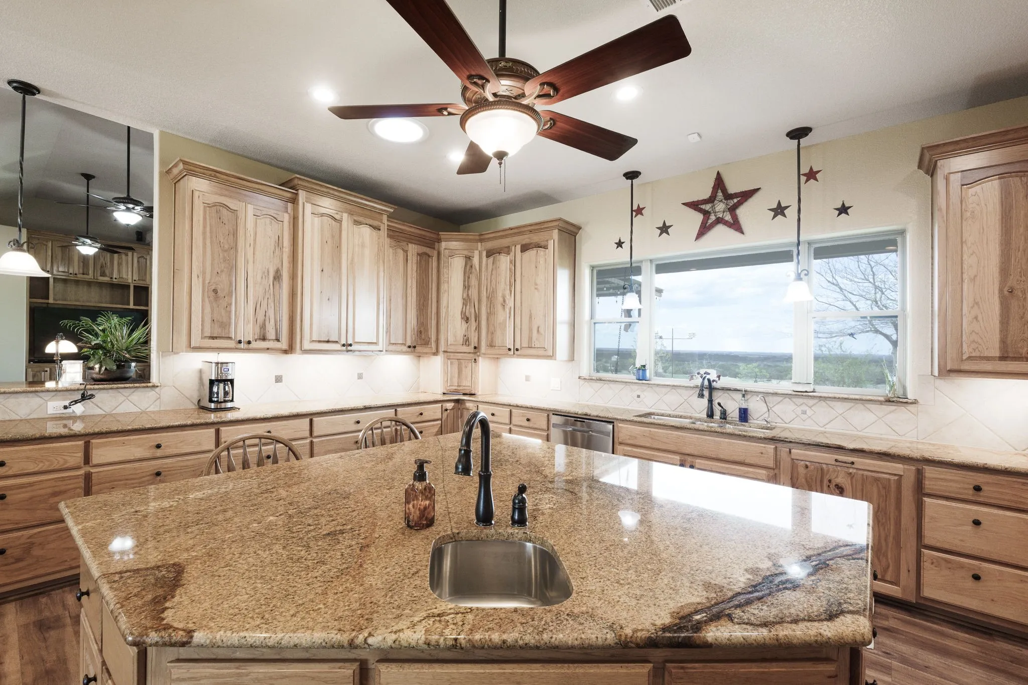 Kitchen featuring a spacious island with an undermount sink and dark-finish faucet, granite countertops, light wood cabinetry, and a white tile backsplash