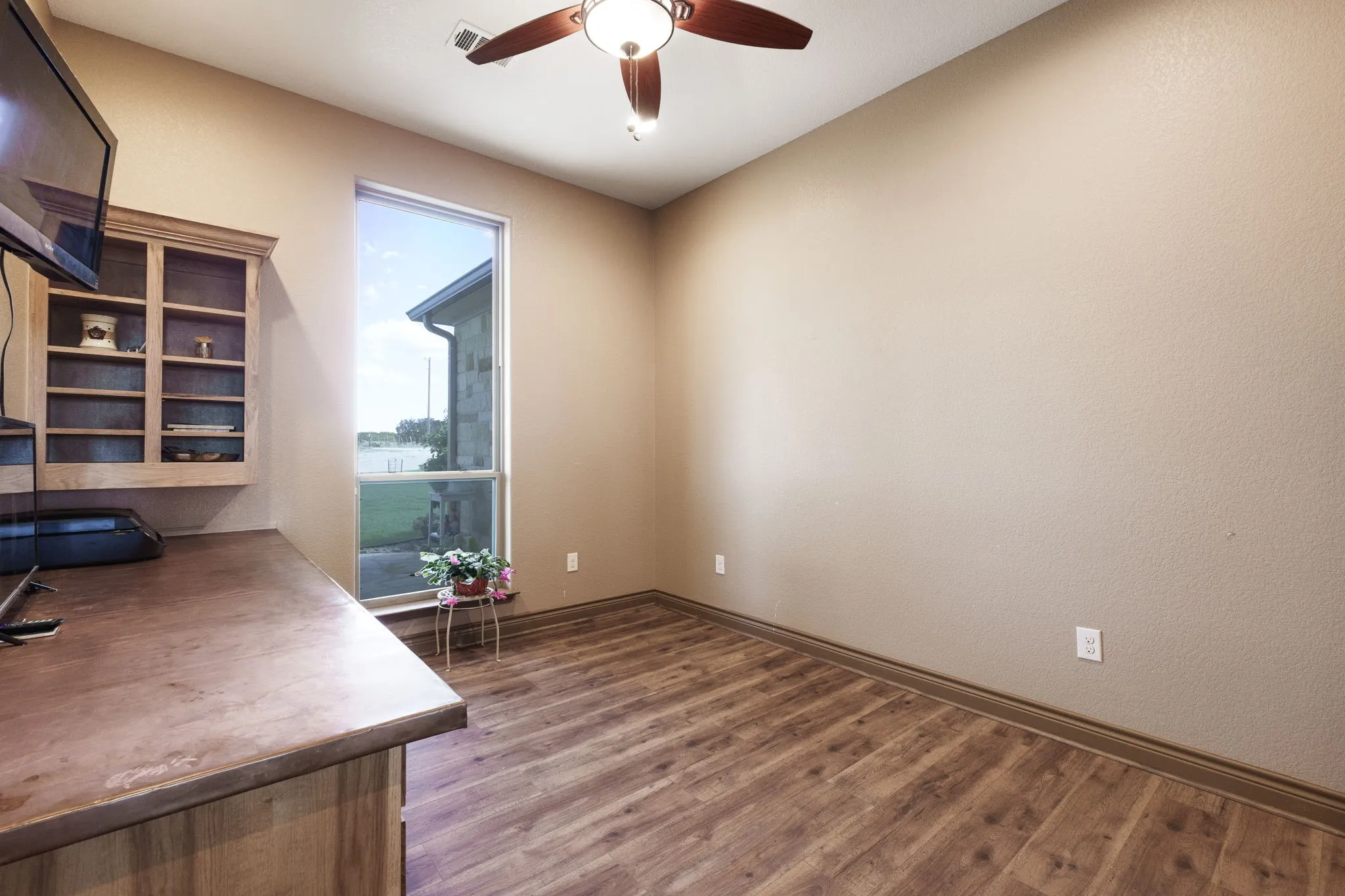 Vertical window offering natural light, complemented by wood-finish flooring and a ceiling fan