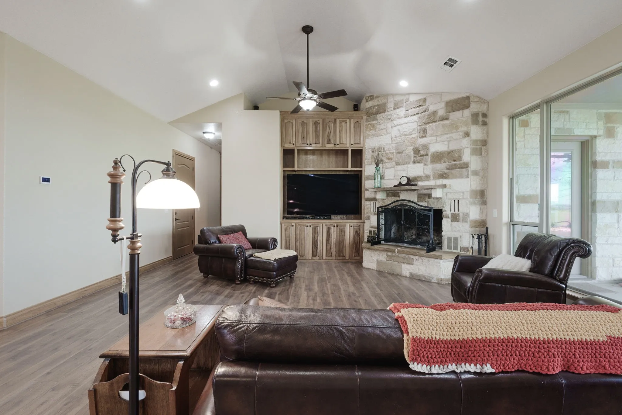 Spacious living area featuring wood-finish flooring, a stone fireplace with hearth, and built-in cabinetry surrounding a media center