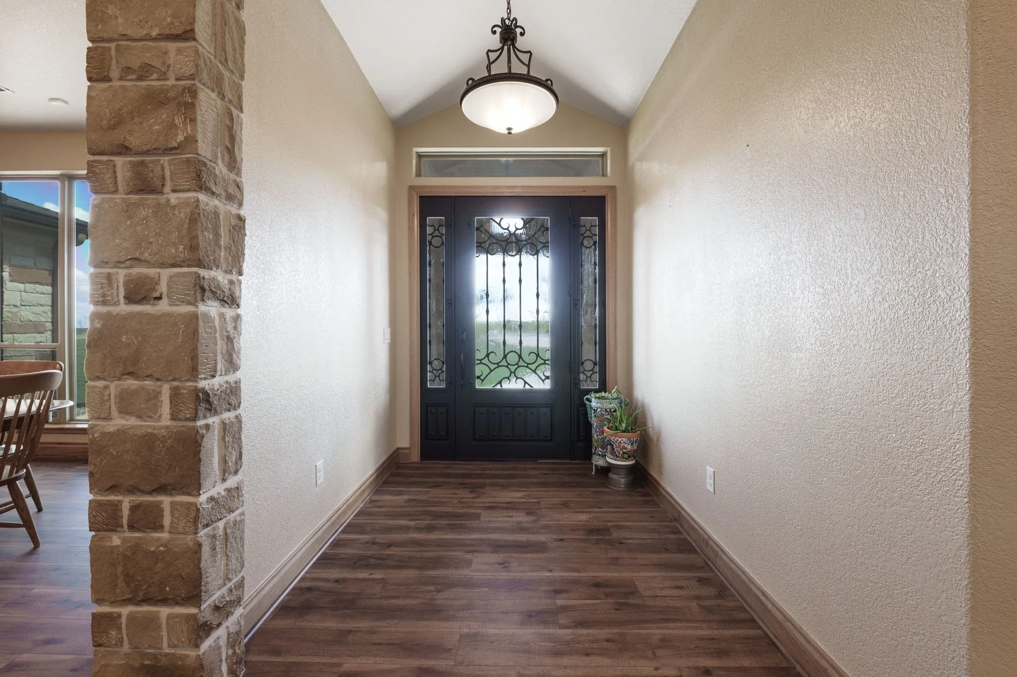 Entryway featuring wood-finish flooring, a stone-clad architectural column, and a vaulted ceiling