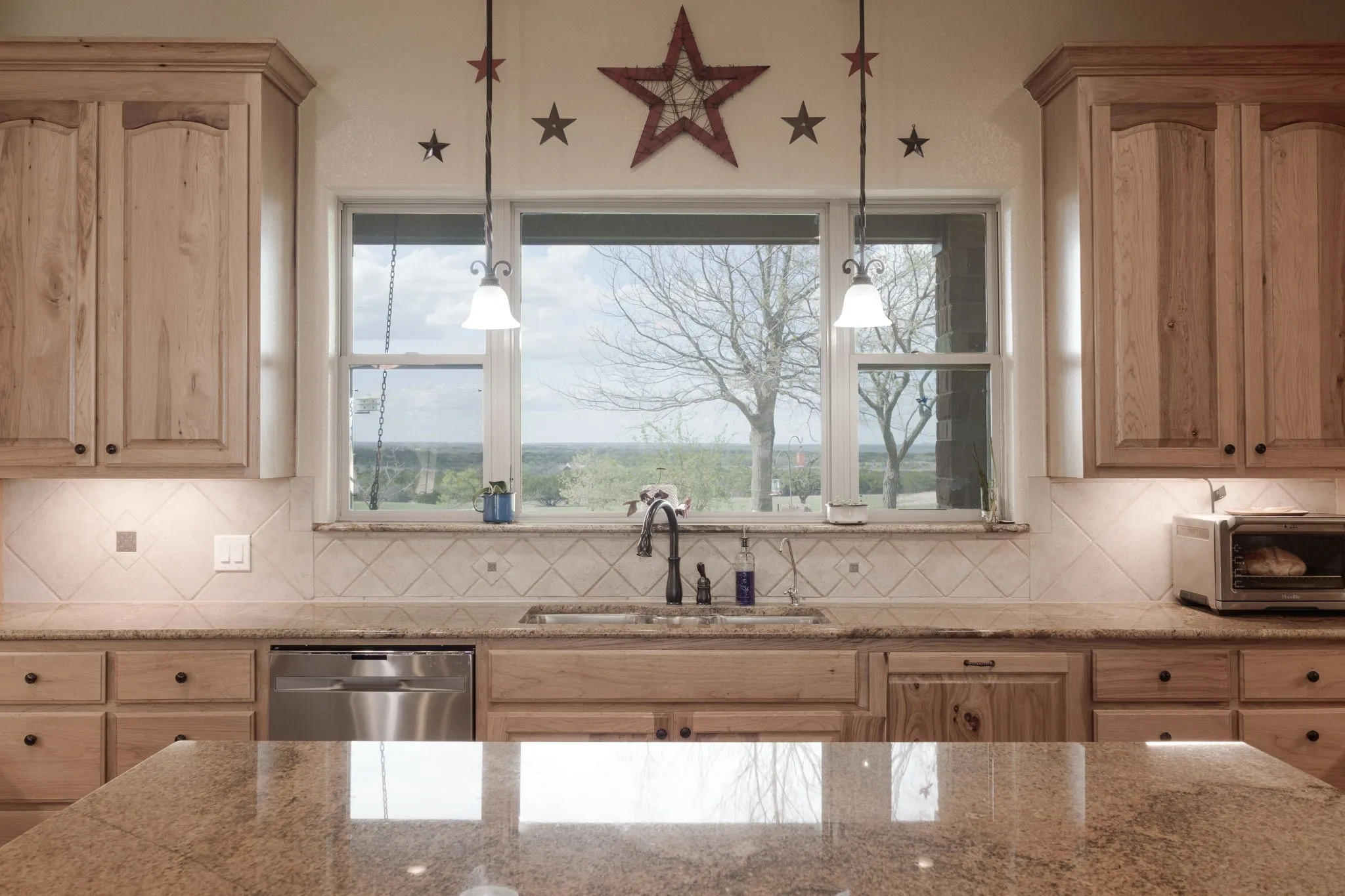 Kitchen featuring natural wood cabinetry with recessed panels, a large window over the sink, stainless steel dishwasher, and polished stone countertops