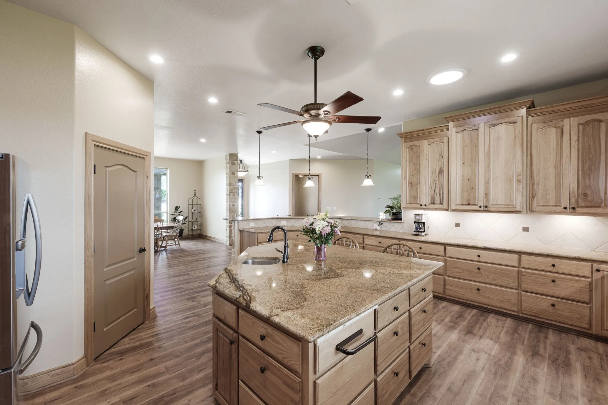 Spacious kitchen featuring a large central island with sink, extensive wood-finish cabinetry, light-toned countertops, and wood-finish flooring