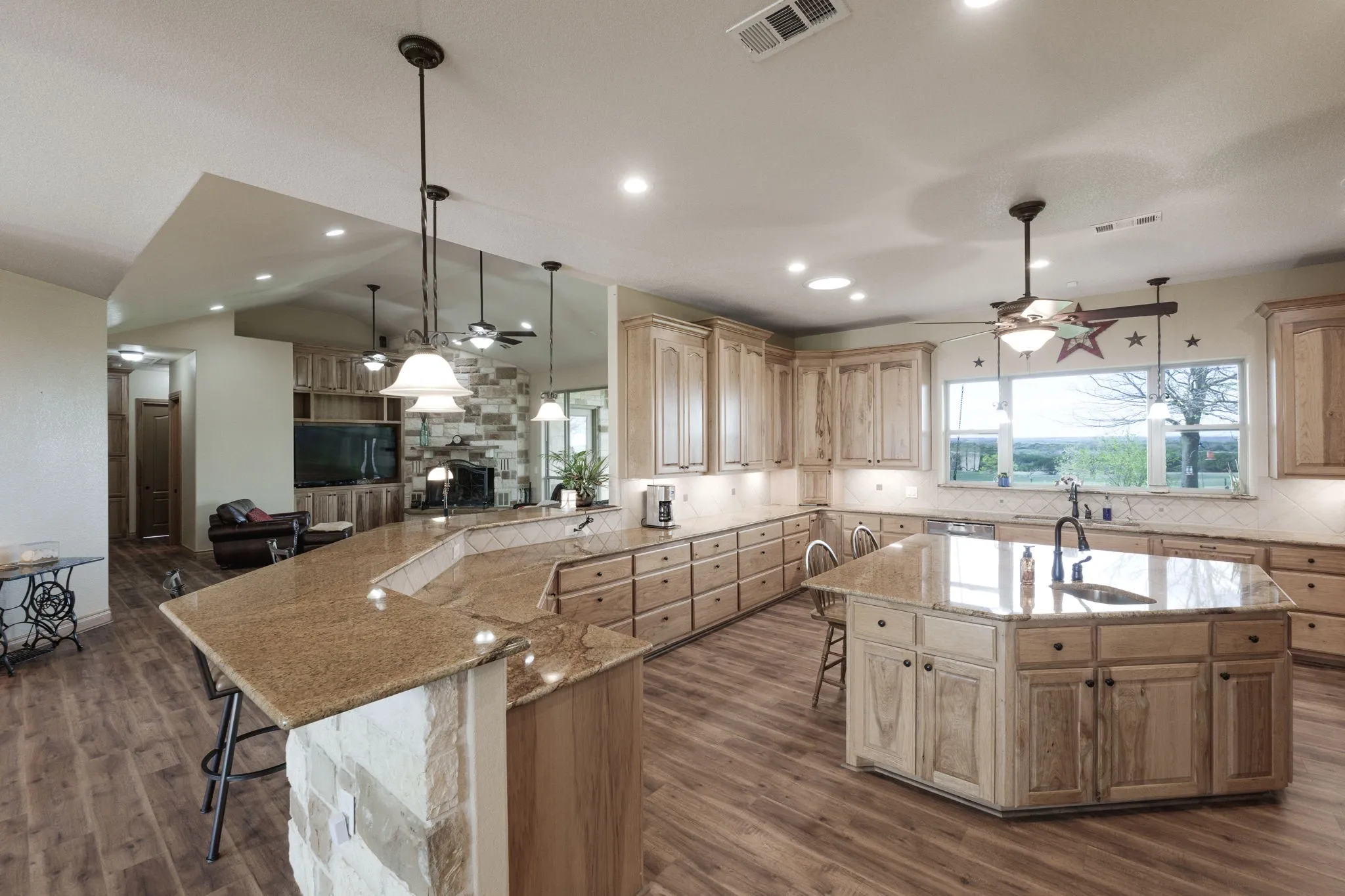 Kitchen featuring extensive light wood cabinetry, stone countertops, a large center island with an undermount sink, recessed lighting, and wood-finish flooring