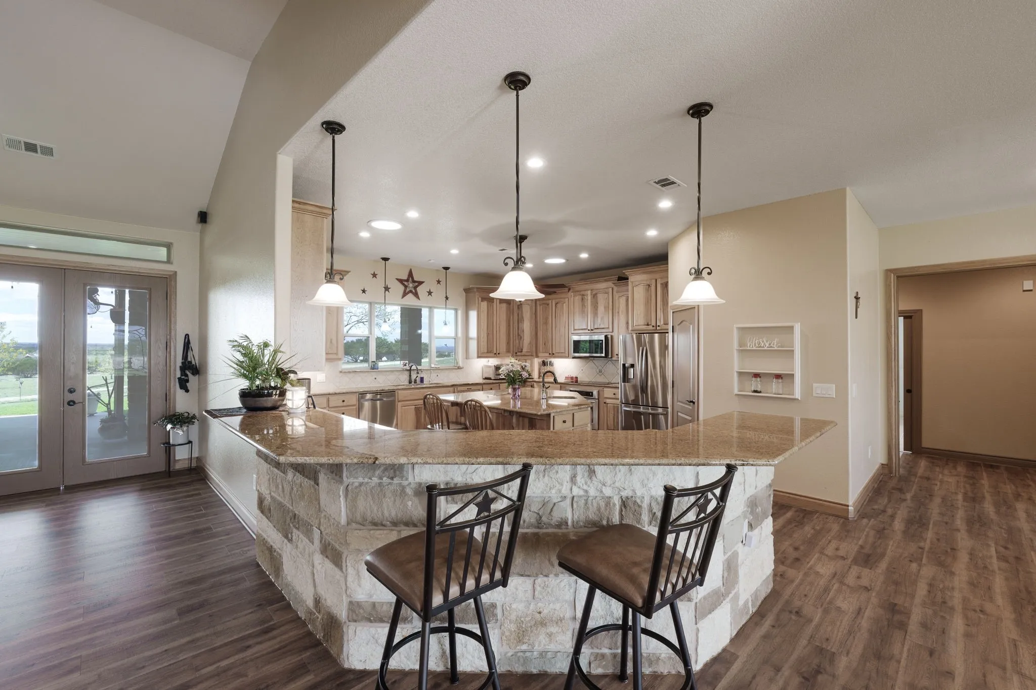Open-concept kitchen featuring granite countertops, wood-finish flooring, recessed lighting, and a stone-faced breakfast bar