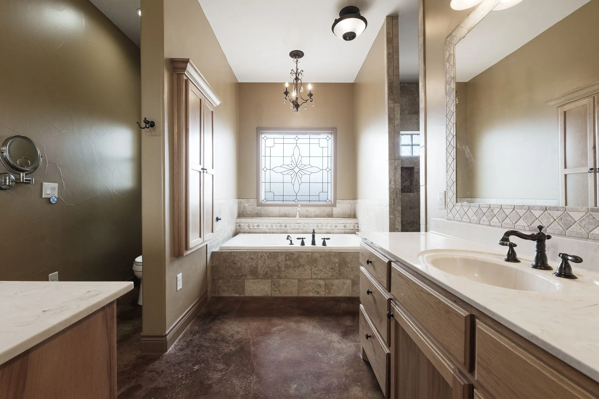 Bathroom featuring a built-in soaking tub with tiled surround, leaded glass window, wood-finish vanity with a white countertop and oval sink, oil-rubbed bronze fixtures, and wood-finish flooring