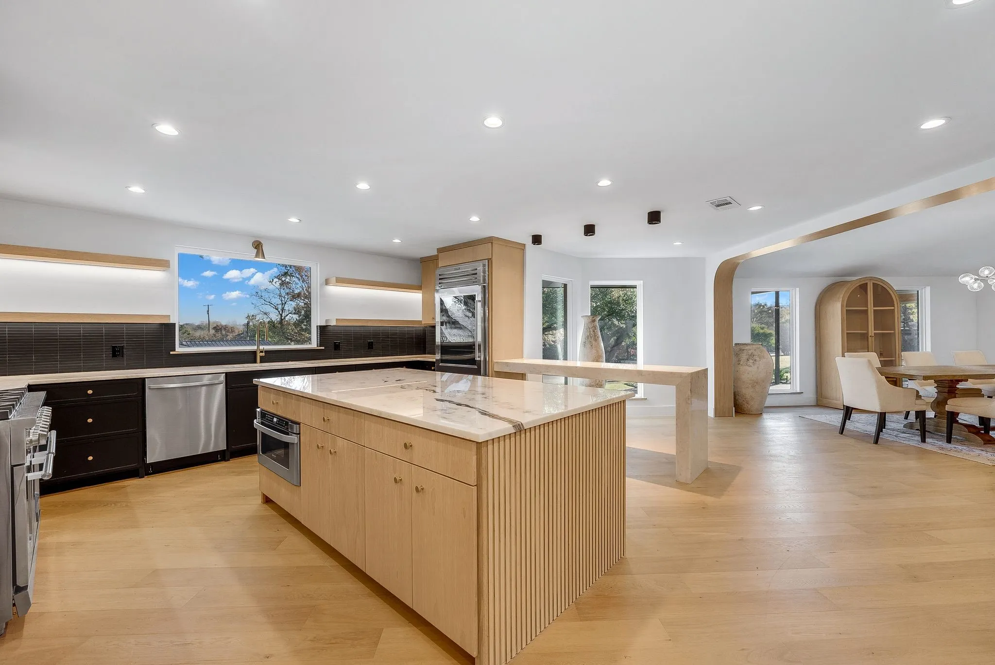 Kitchen with light brown cabinets, a kitchen island, light stone counters, light wood-style flooring, and recessed lighting
