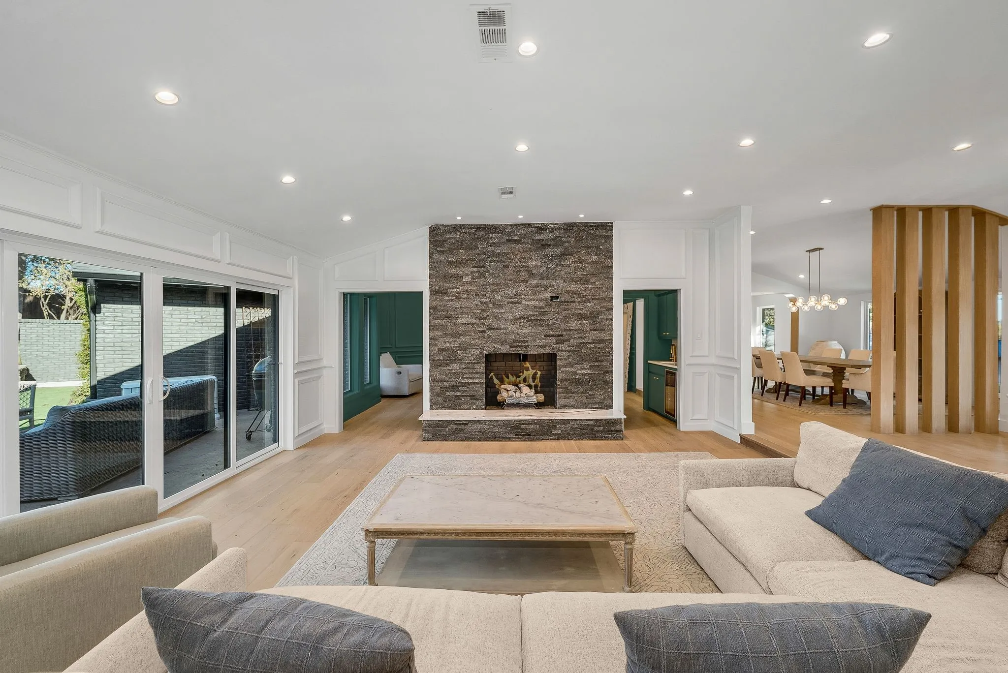 Living area featuring a stone fireplace, a decorative wall, lofted ceiling, light wood-style flooring, and recessed lighting