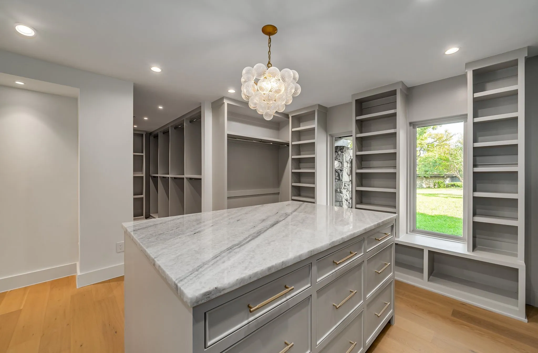 Walk in closet with light wood finished floors and a chandelier