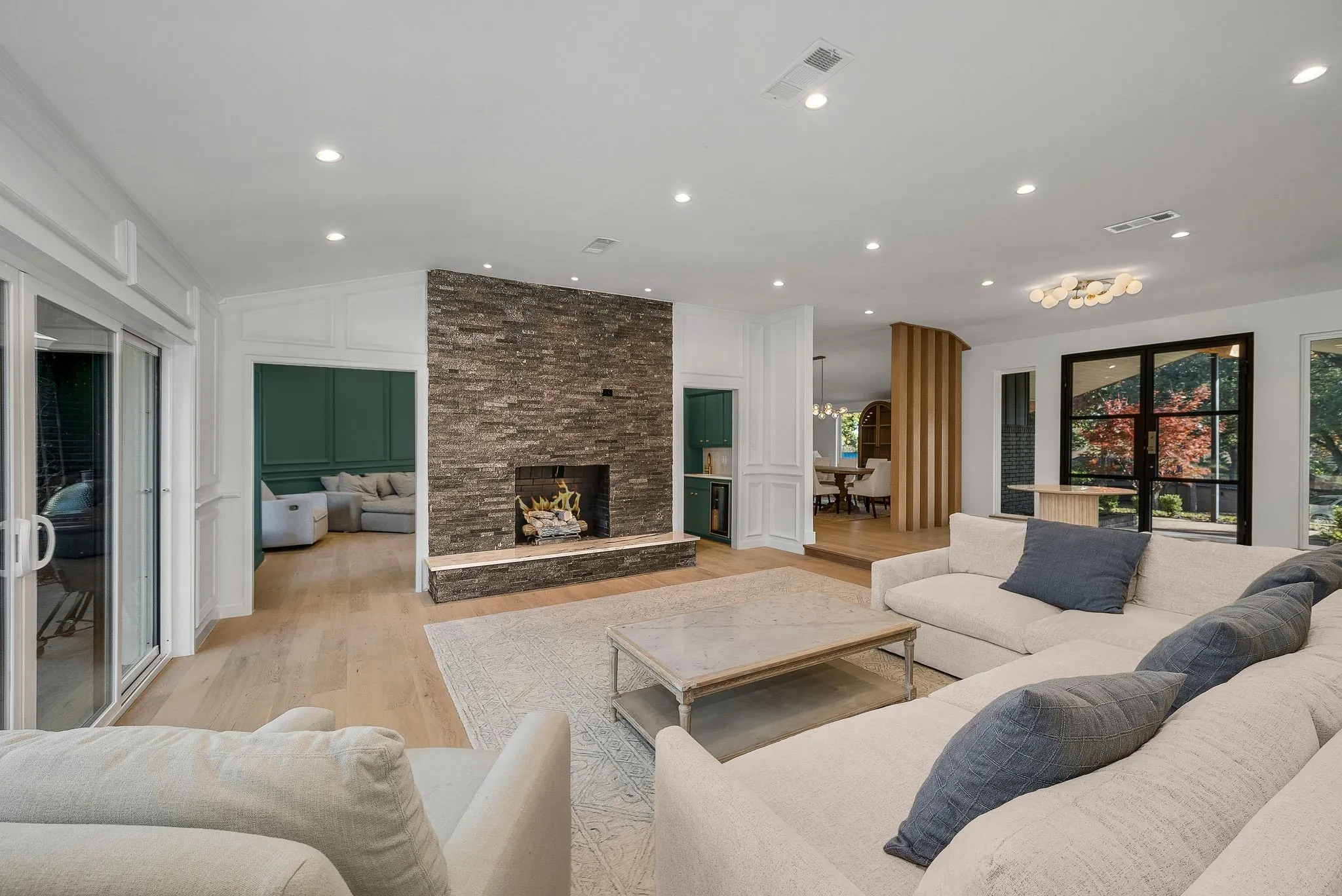 Living area with light wood-type flooring, a stone fireplace, recessed lighting, vaulted ceiling, and a decorative wall