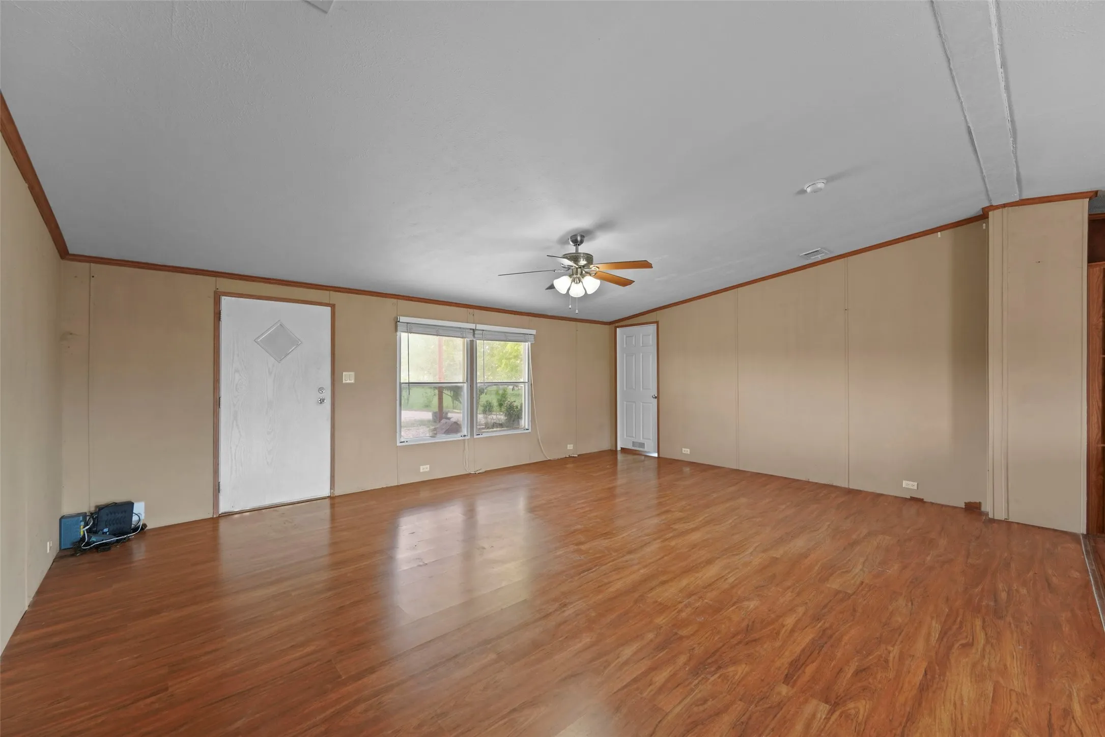 Spacious interior room featuring wood-finish flooring, neutral wall paneling, and a ceiling fan with integrated lighting