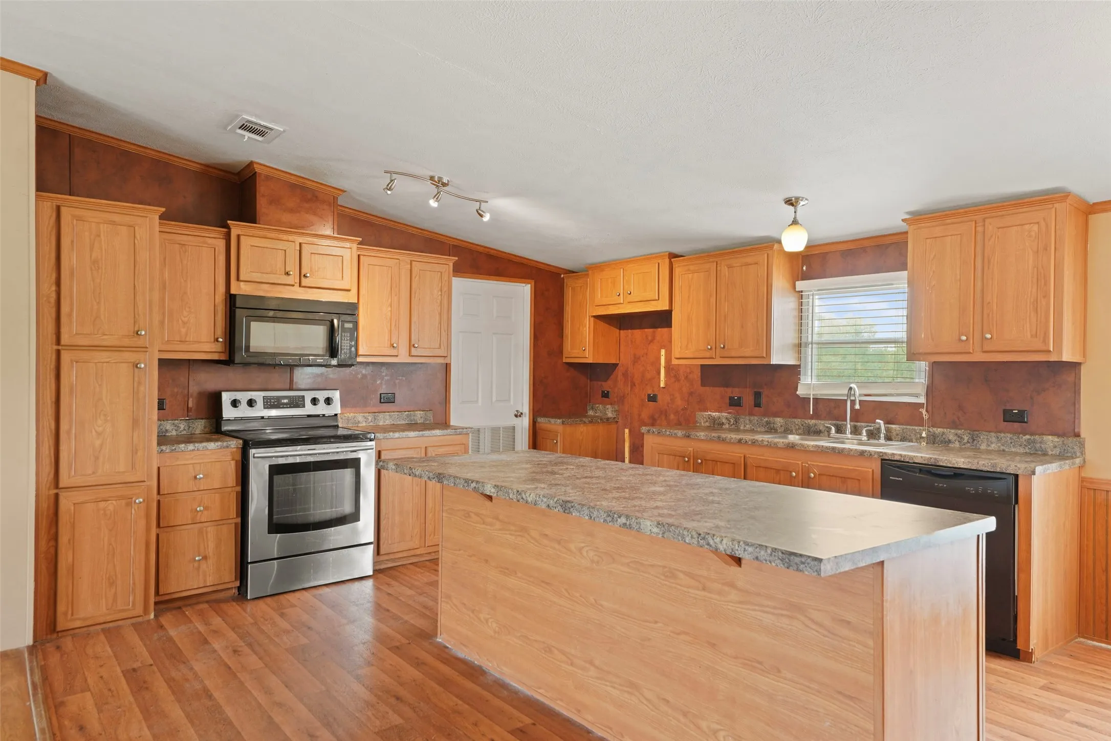 Kitchen featuring a central island with a laminate countertop, wood-finish flooring, light wood cabinetry, stainless steel range, and a built-in microwave