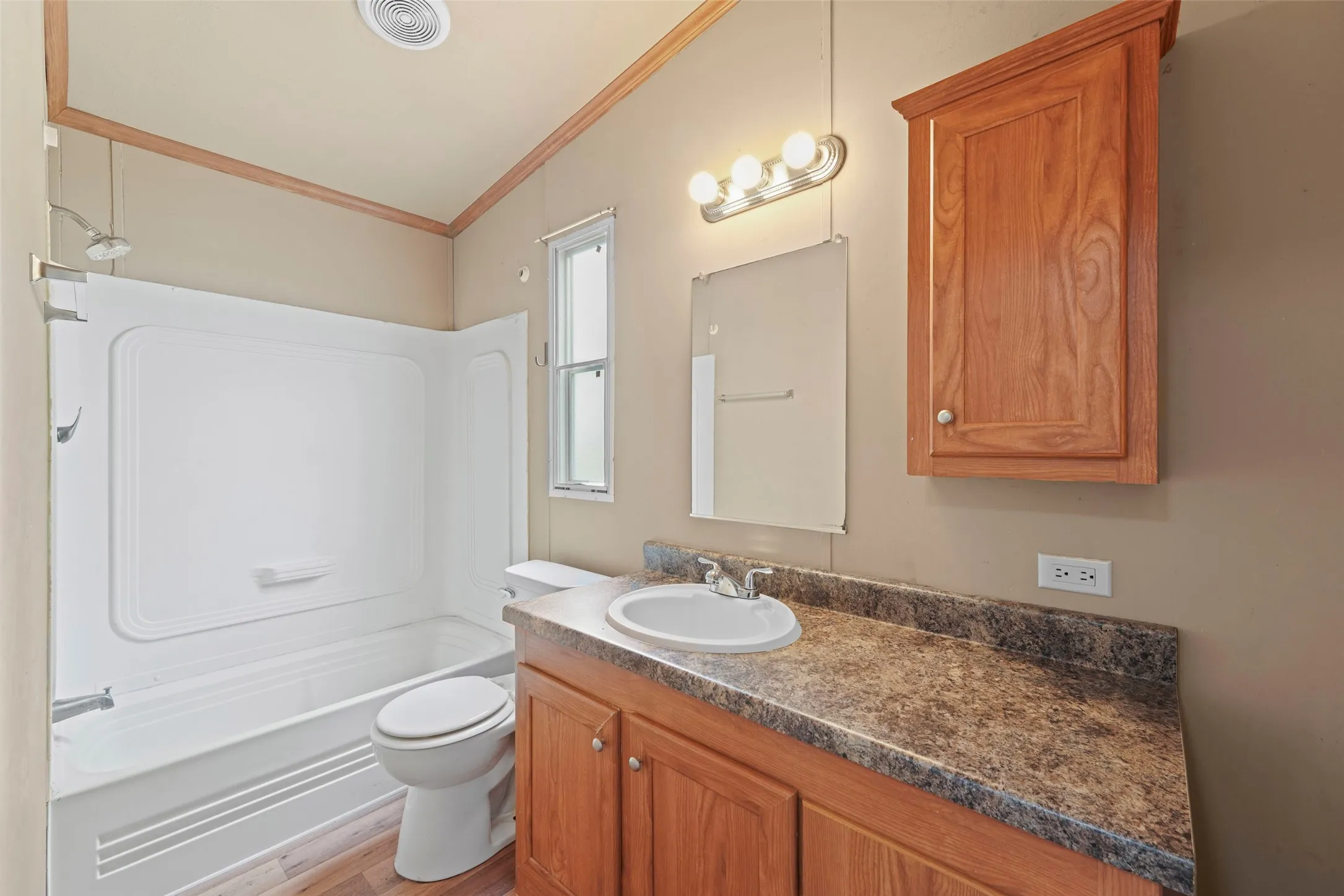 Bathroom featuring a white tub and shower combination, wood-finish vanity with a single basin sink, and a mounted wood-finish cabinet